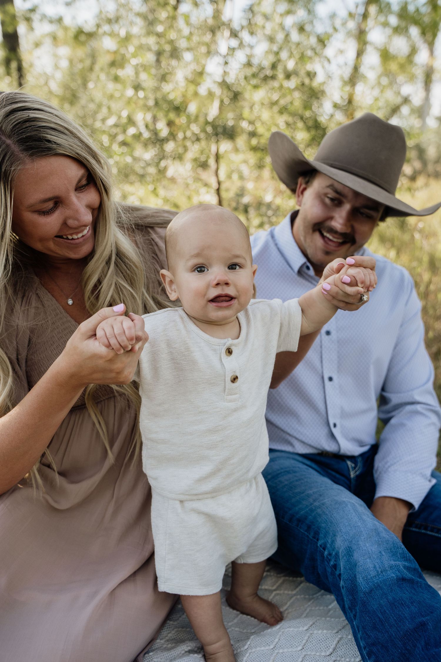 Happy family with baby standing between smiling parents in outdoor photo session.