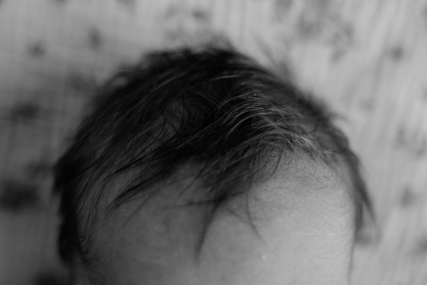 Black and white close-up of a newborns dark hair against a patterned blanket.