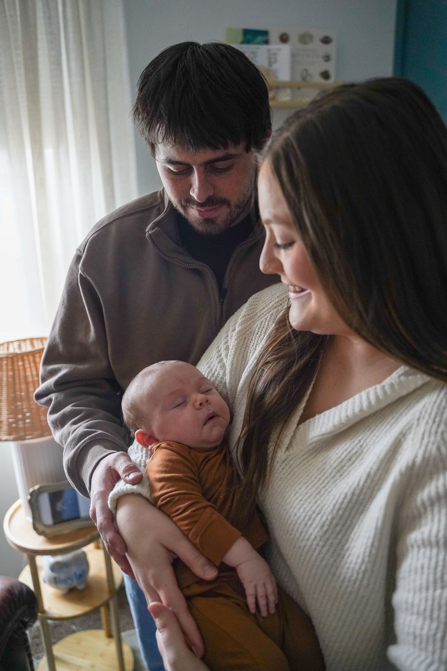 New parents smiling lovingly at their sleeping newborn baby wrapped in orange swaddle.