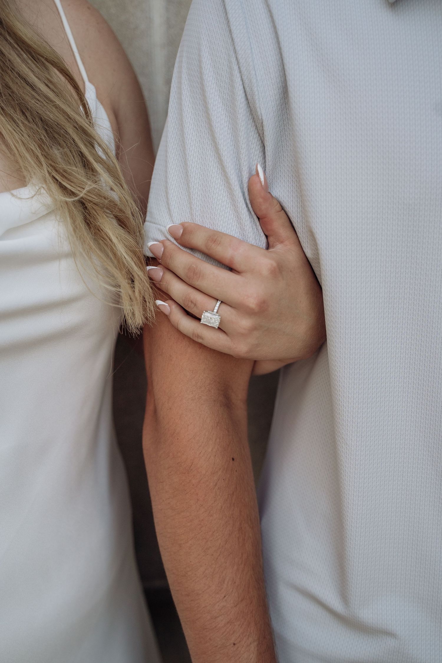 Close-up of womans hand with large emerald-cut diamond engagement ring holding mans arm.