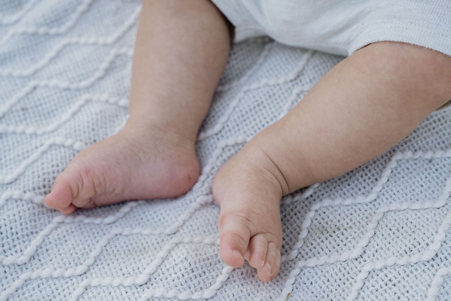 Close-up of cute baby feet resting on a soft white knitted blanket with diamond pattern texture.