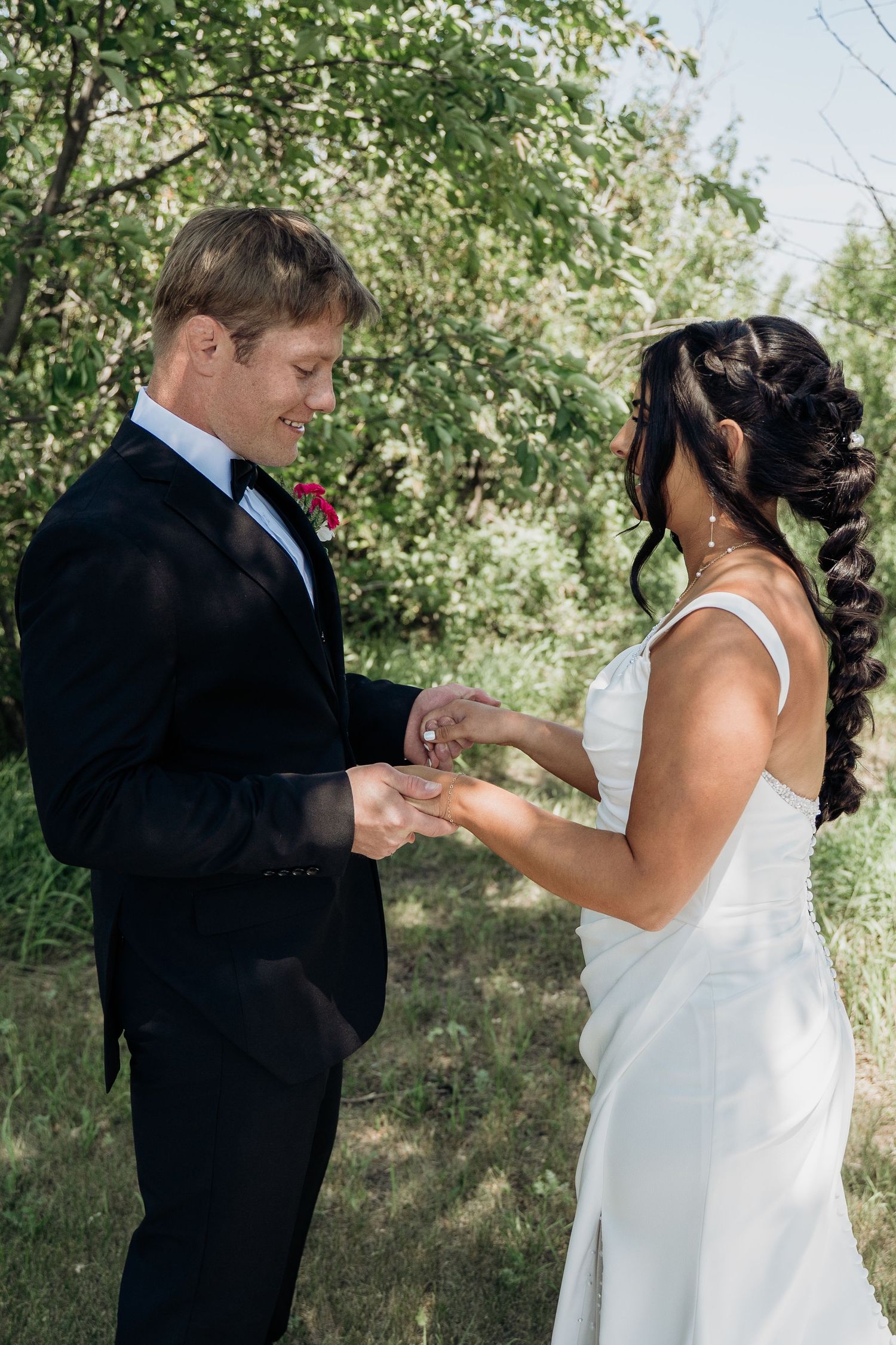 Groom places wedding ring on brides finger during outdoor ring exchange ceremony.