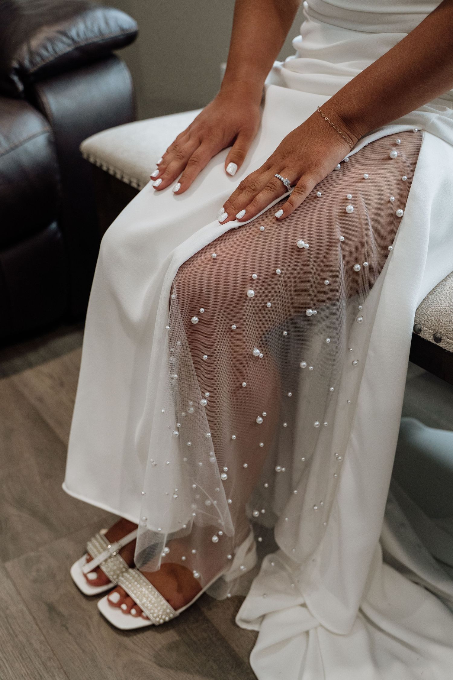 Bride in white wedding dress with pearl-embellished tulle overlay sitting with manicured hands on her lap.