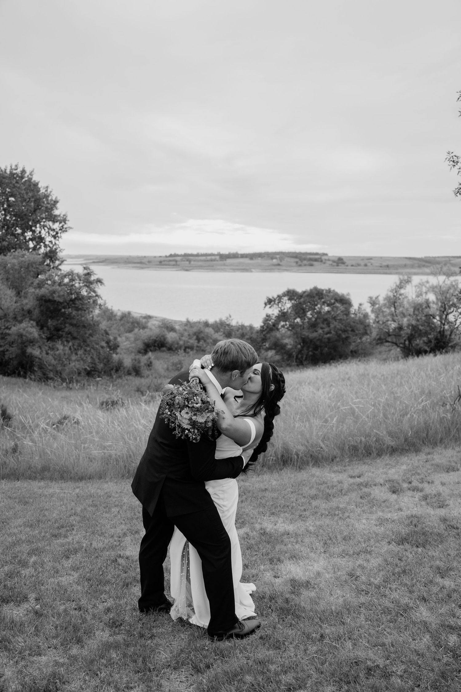 Black and white photo of bride and groom sharing a romantic dip kiss in a grassy field.