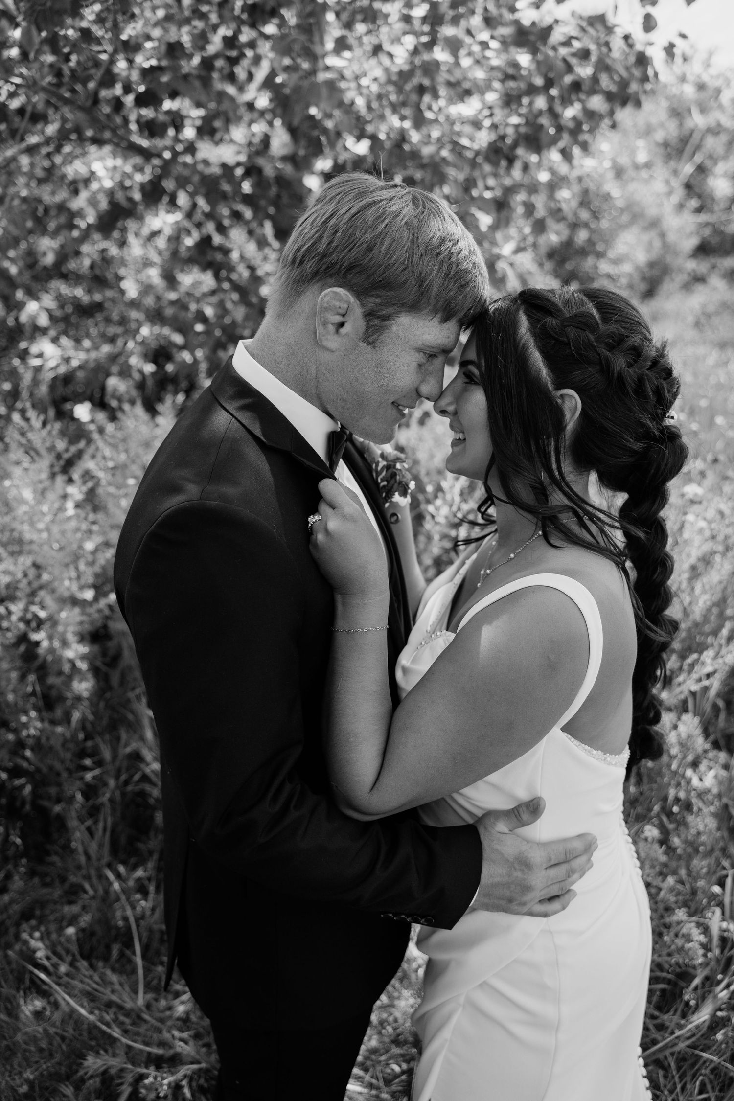 Black and white romantic portrait of bride and groom embracing forehead to forehead in a garden setting.