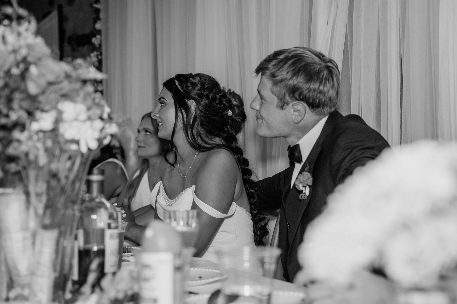 Bride and groom seated at wedding reception table in black and white photo.