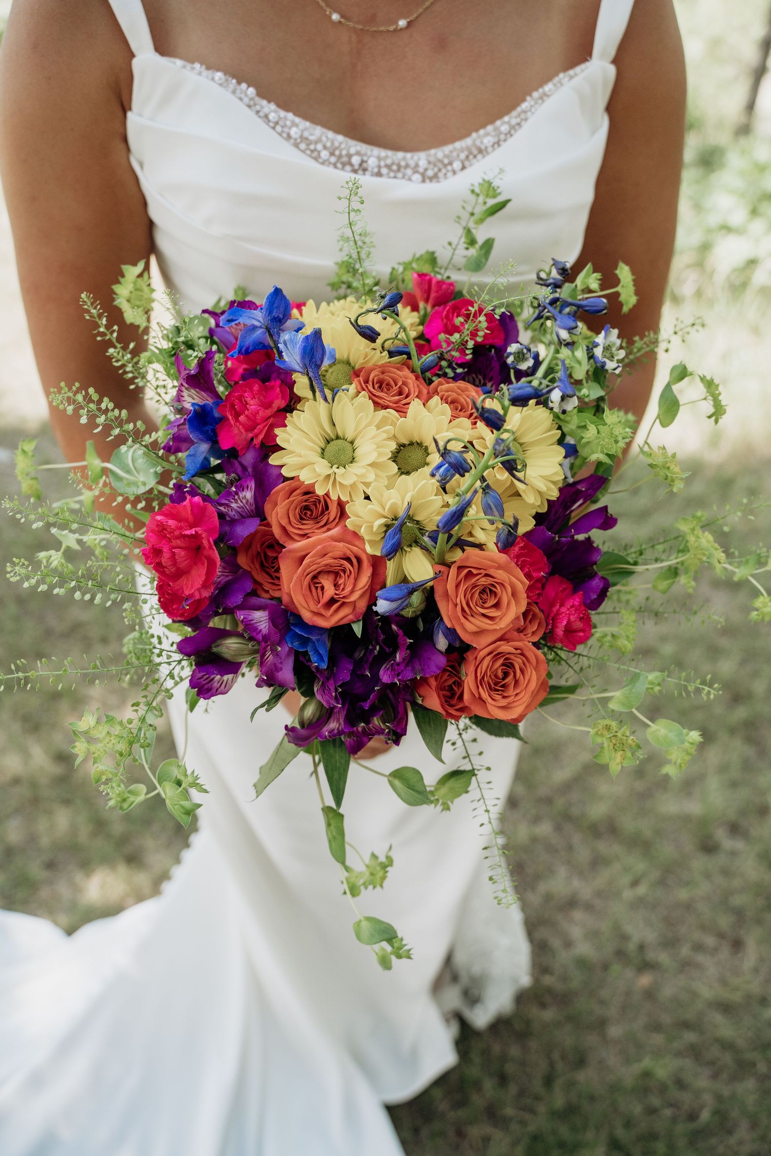 Bride holding vibrant wedding bouquet with orange roses, purple flowers, and yellow gerbera daisies.