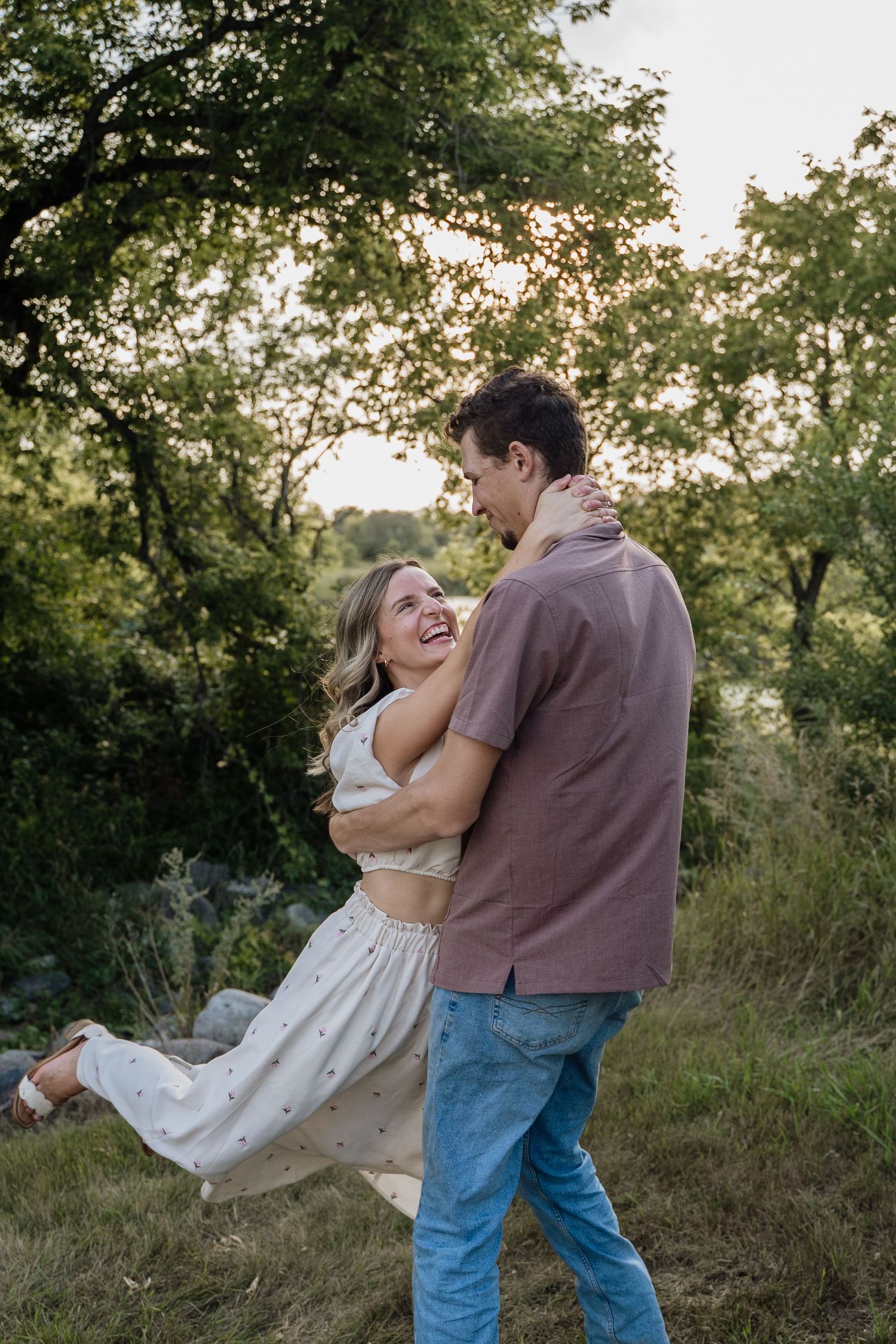 Joyful couple dancing and laughing together outdoors in lush green park at sunset.