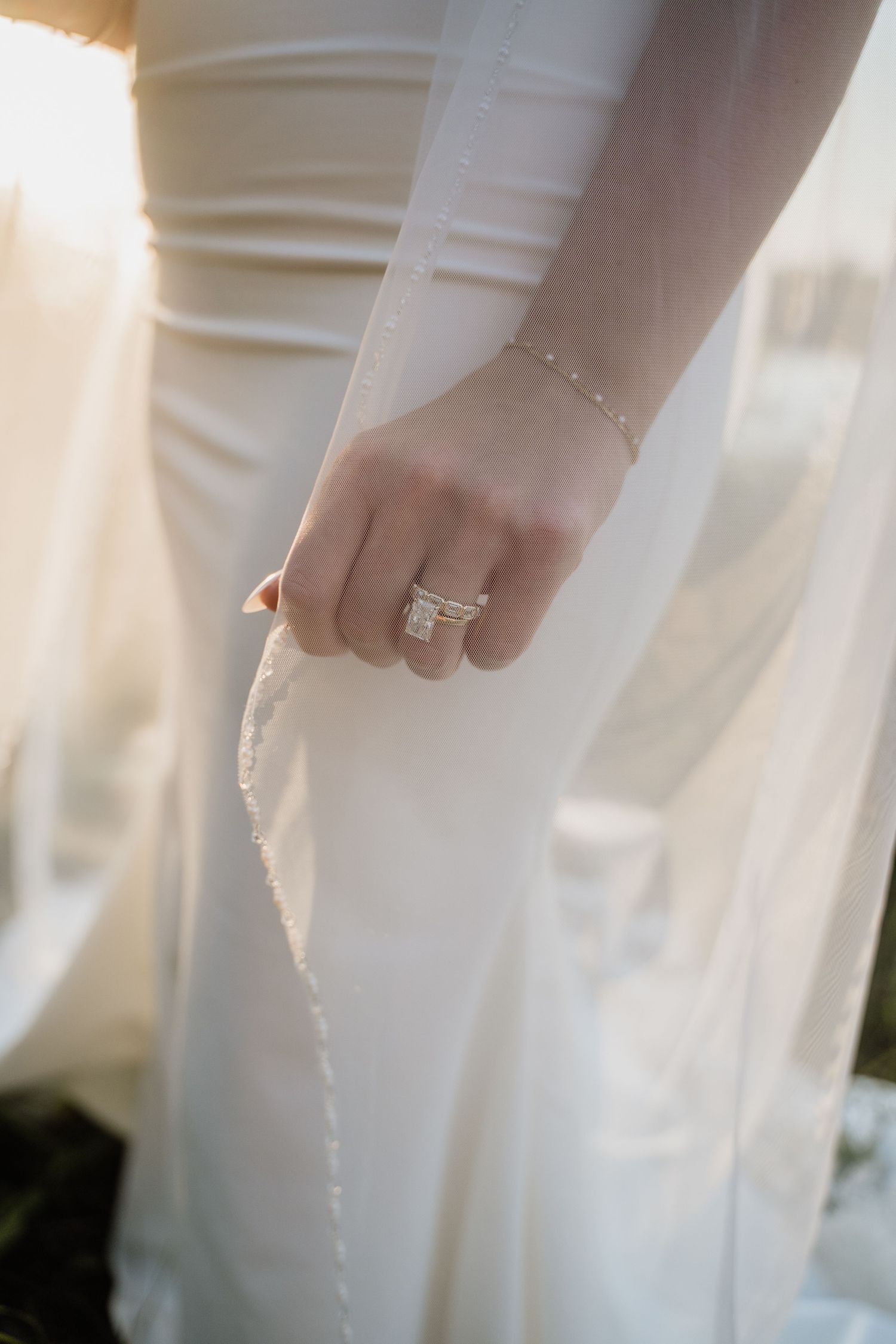 Close-up of bride holding wedding veil wearing elegant diamond engagement ring and delicate gold bracelet.