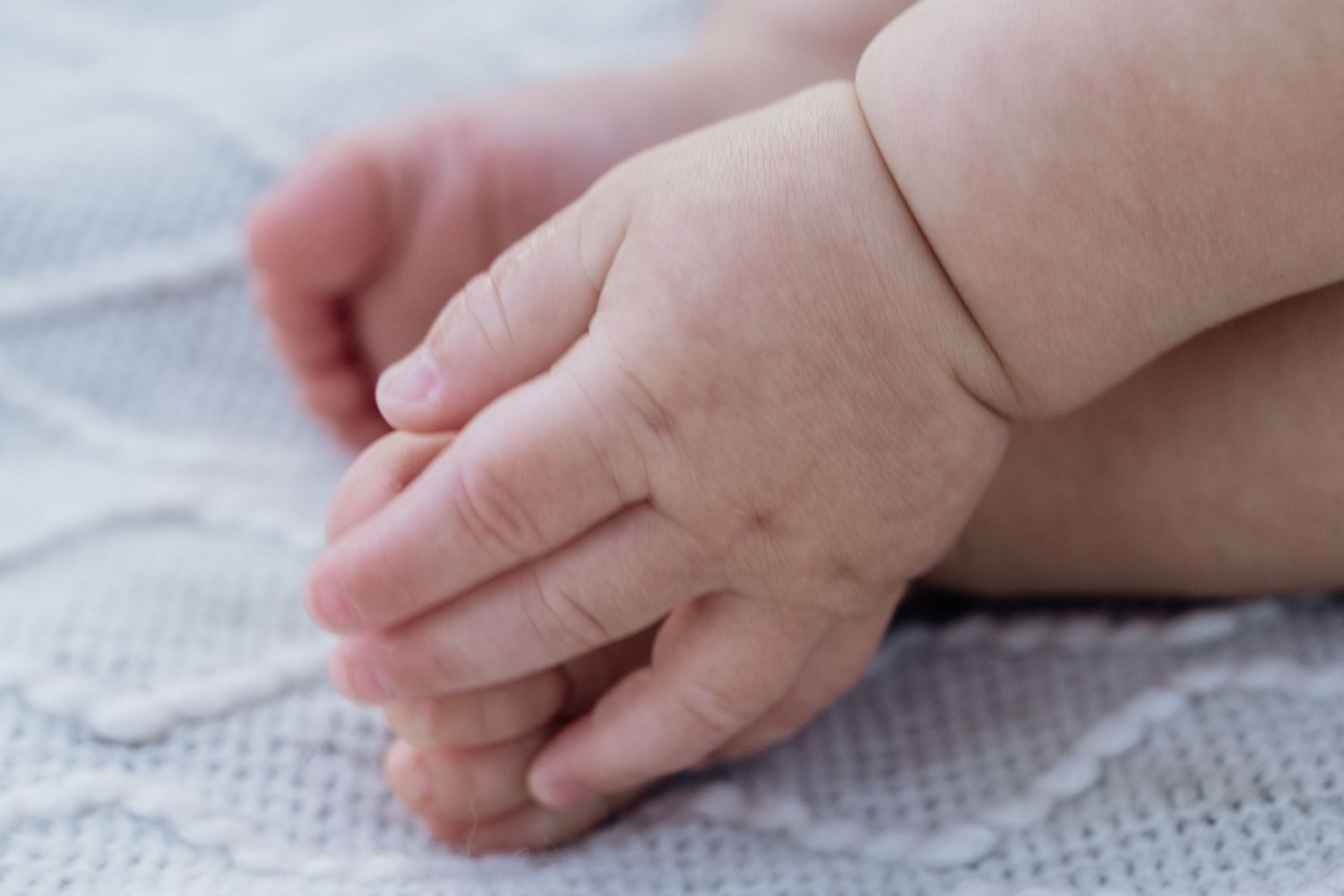 Close-up of a newborn baby's tiny hands resting on a soft white knitted blanket.