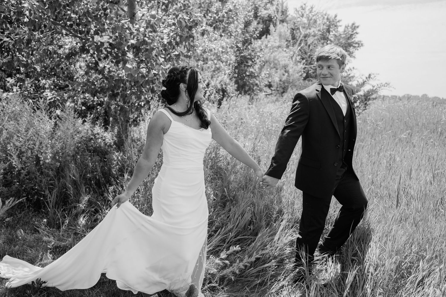 Black and white photo of bride and groom holding hands walking through a field on their wedding day.