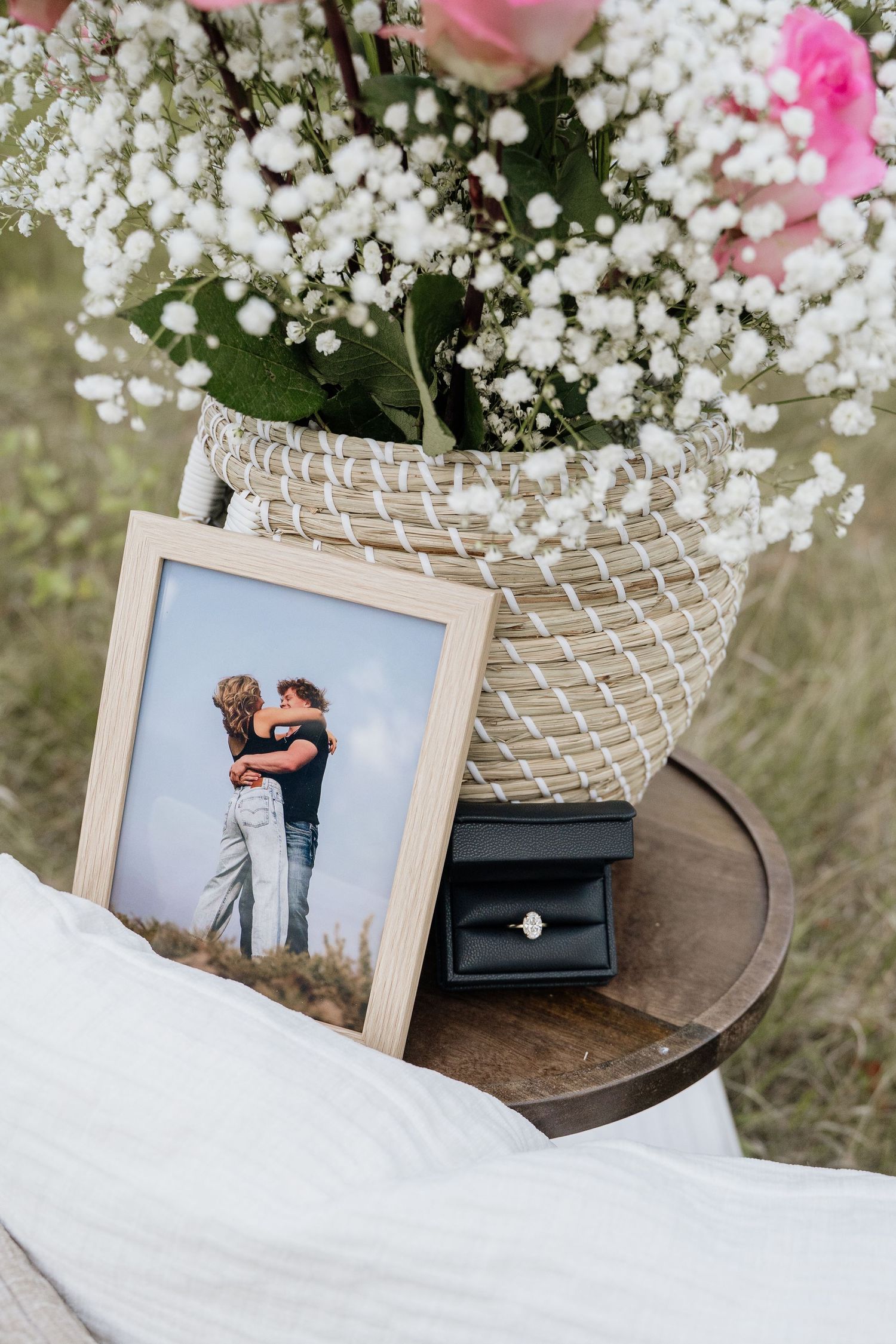 Romantic proposal setup with framed couple photo, diamond ring box, and floral arrangement with pink roses and baby's breath.