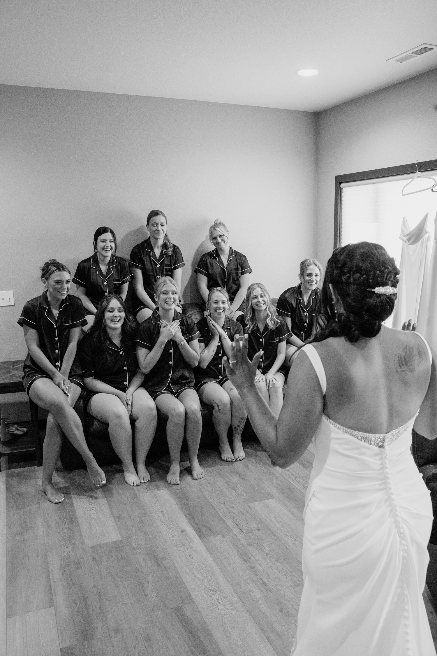 Black and white photo of bridesmaids in matching pajamas reacting to bride revealing her wedding dress.