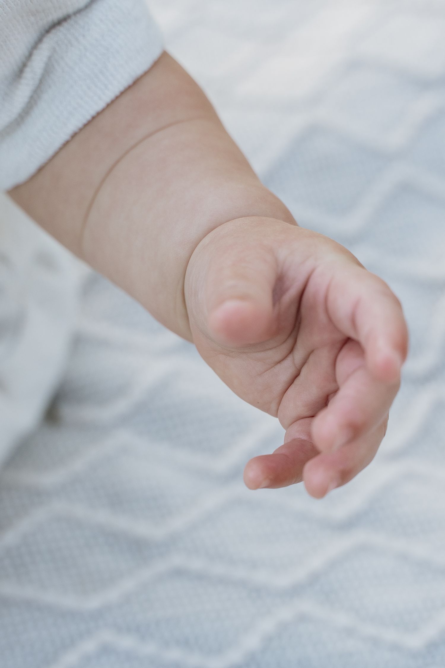 Close-up of a tiny newborn baby hand with delicate fingers, resting gently against a soft white textured blanket.