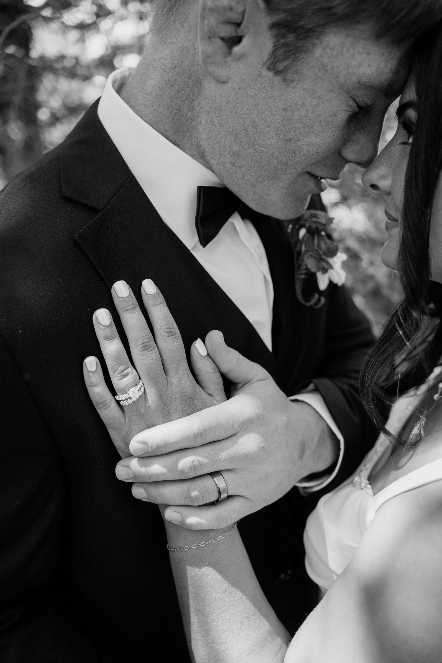 Black and white close-up of bride and groom almost kissing with wedding rings visible on hands.