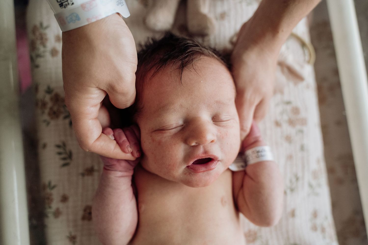 Newborn baby sleeping peacefully in hospital crib while parents gently cradle its head with loving hands.