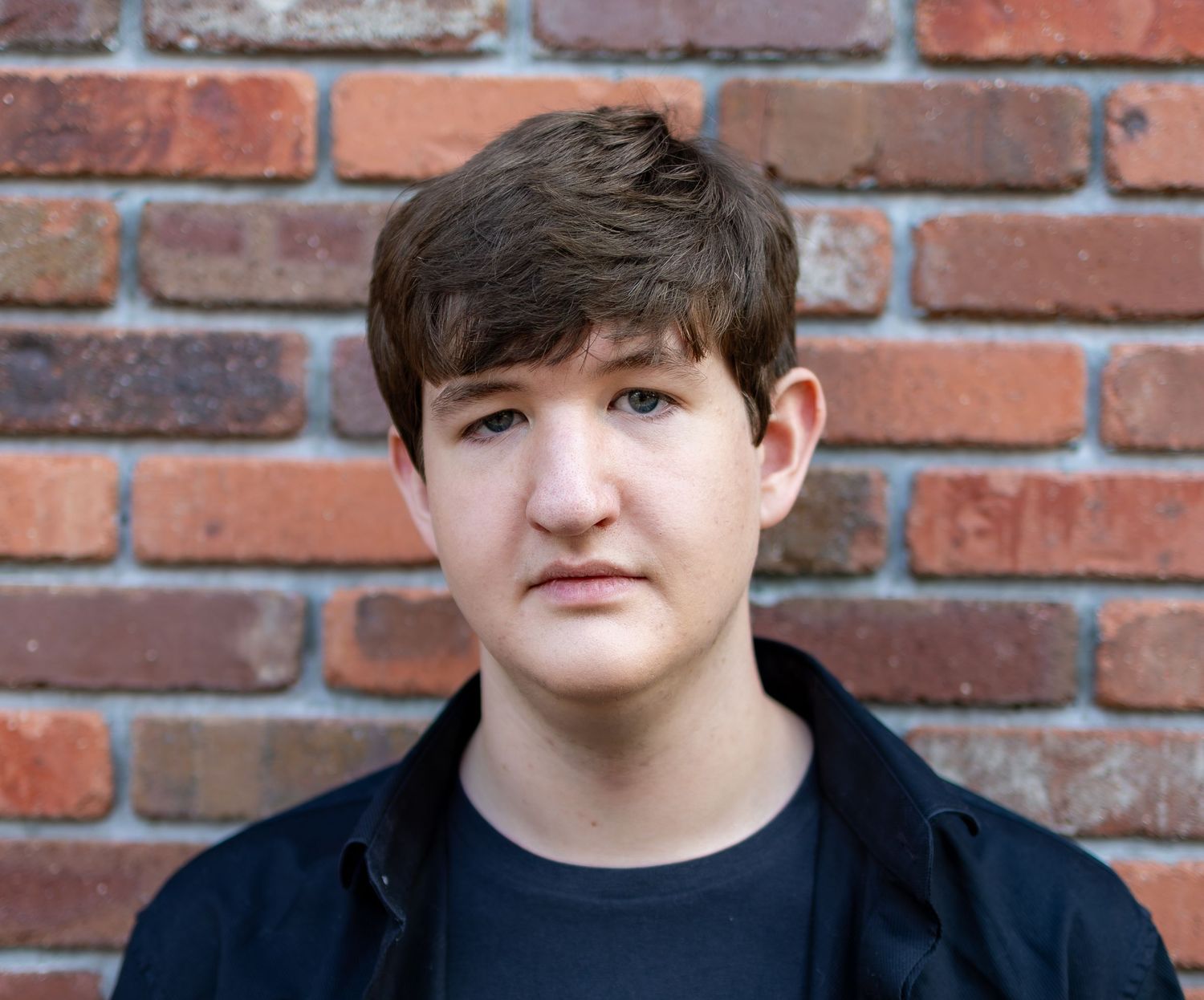 A series of four headshots against a brick wall background with similar poses and lighting.