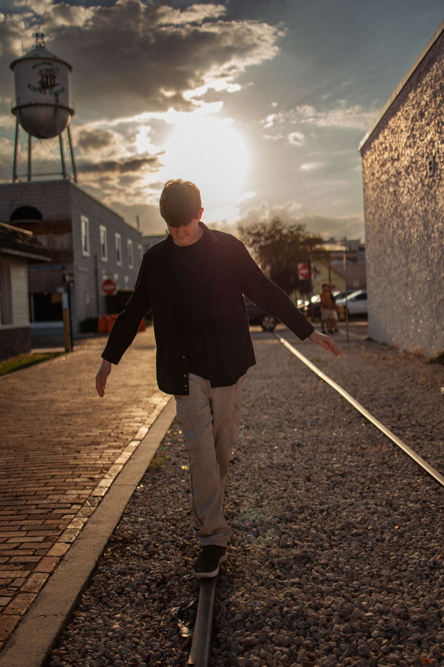 A person balances on a railway track at sunset while walking along gravel and brick path.