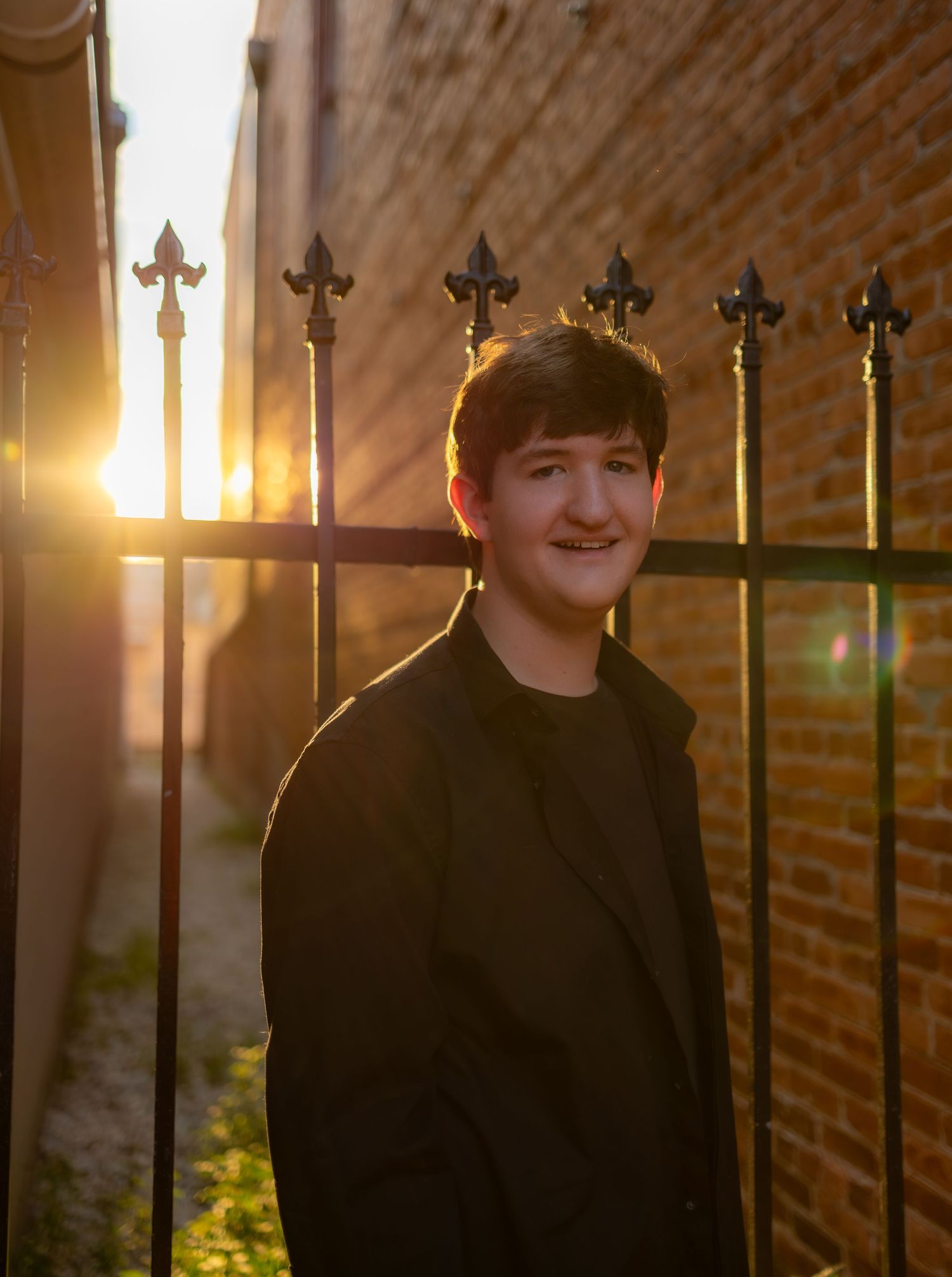 A portrait against a brick wall with golden sunlight streaming through decorative iron railings at sunset.