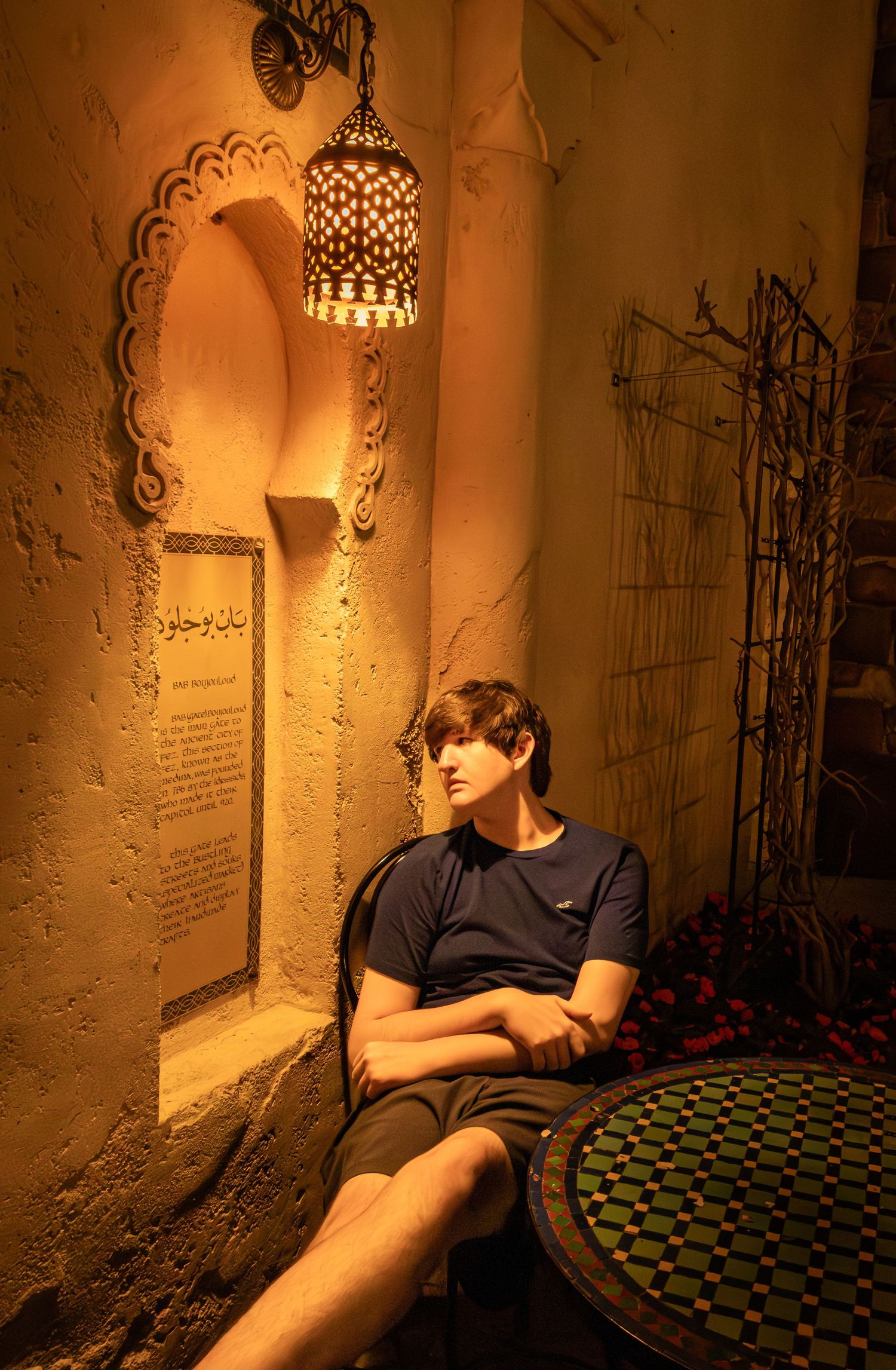 Person resting on floor in dimly lit room with ornate wall decor and hanging lantern creating warm ambiance.