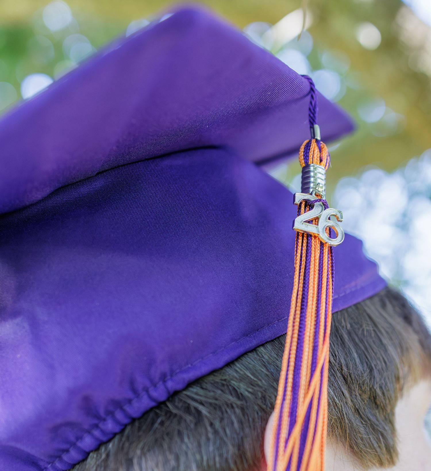 Close-up of a purple graduation cap with orange and purple tassel featuring a 2023 charm on a graduate.