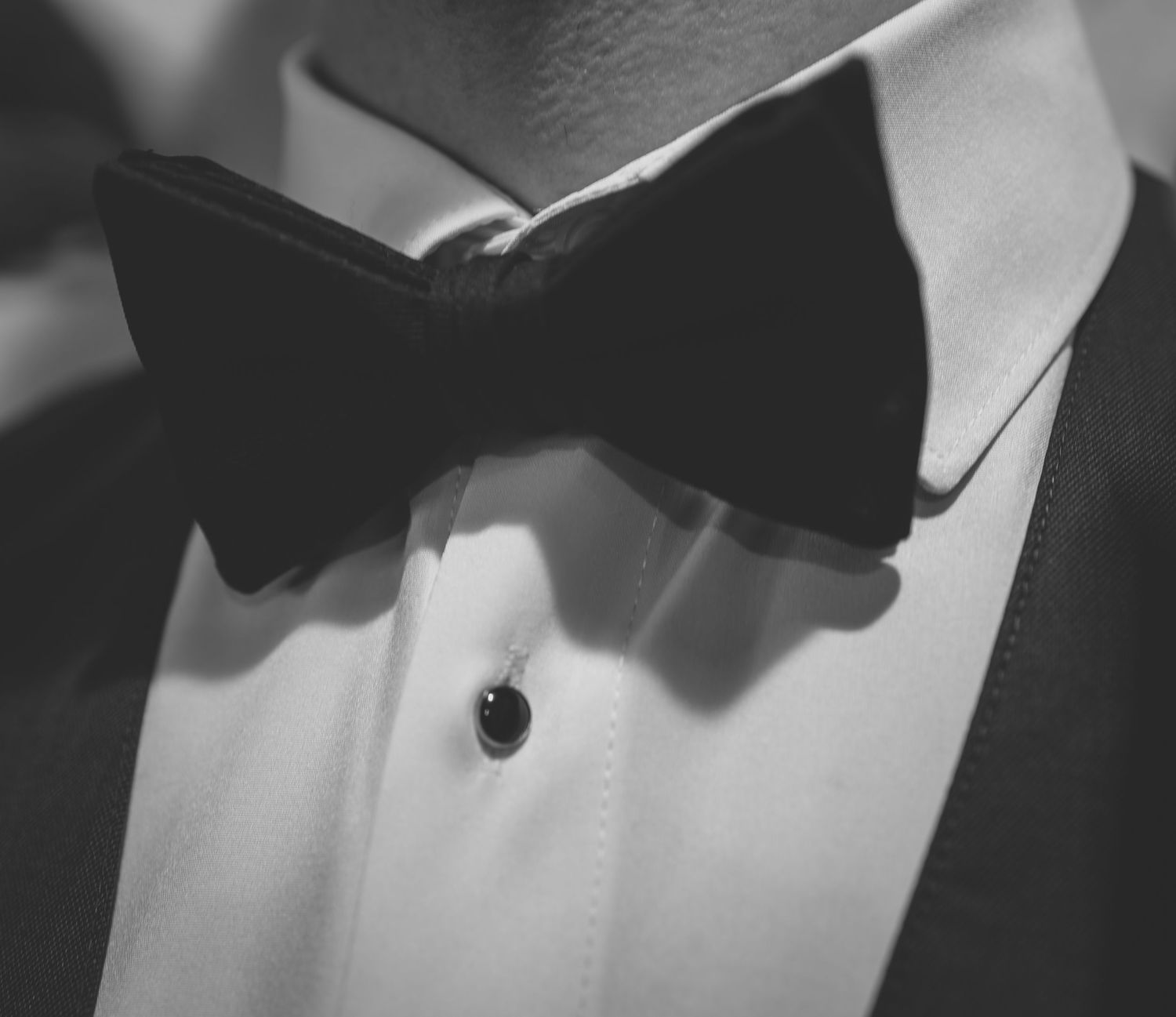 Close-up black and white photo of a man wearing a tuxedo with a black bow tie and shirt stud.