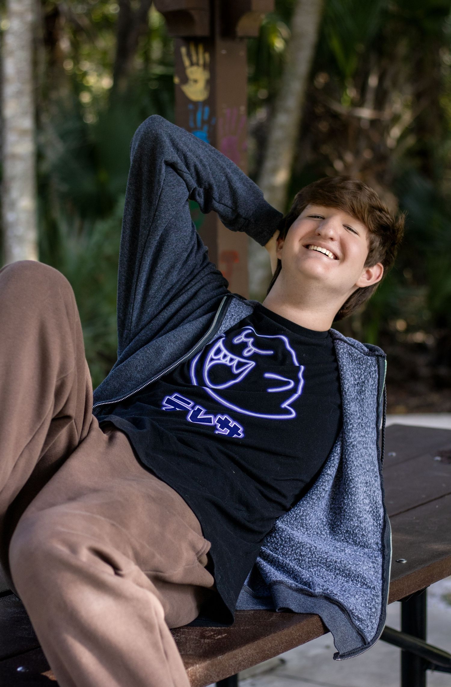 A collage of four photos showing a navy t-shirt with a purple cat design being modeled on a wooden bench outdoors.