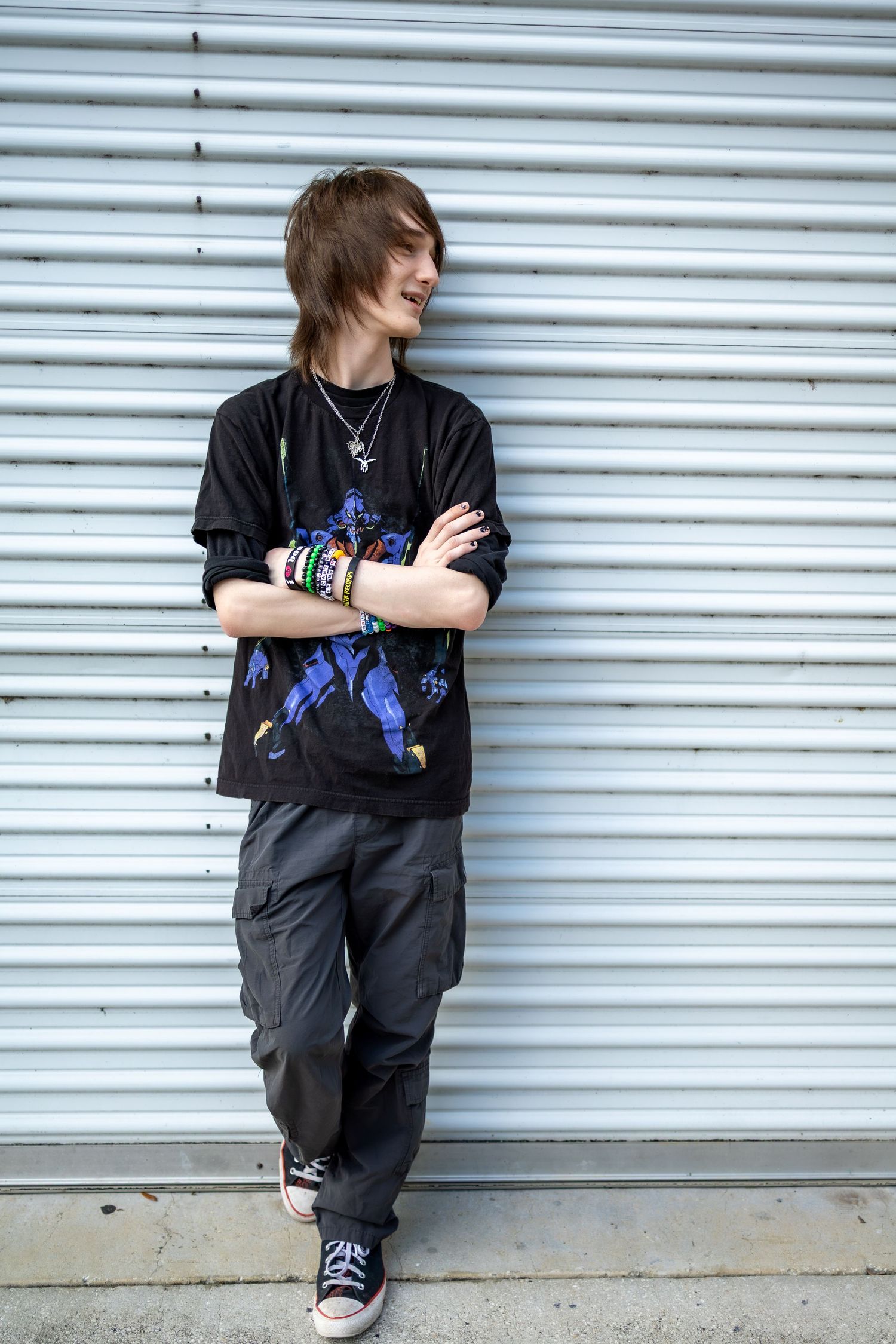 Person in dark clothing leans casually against metal garage door wearing colorful wristbands.