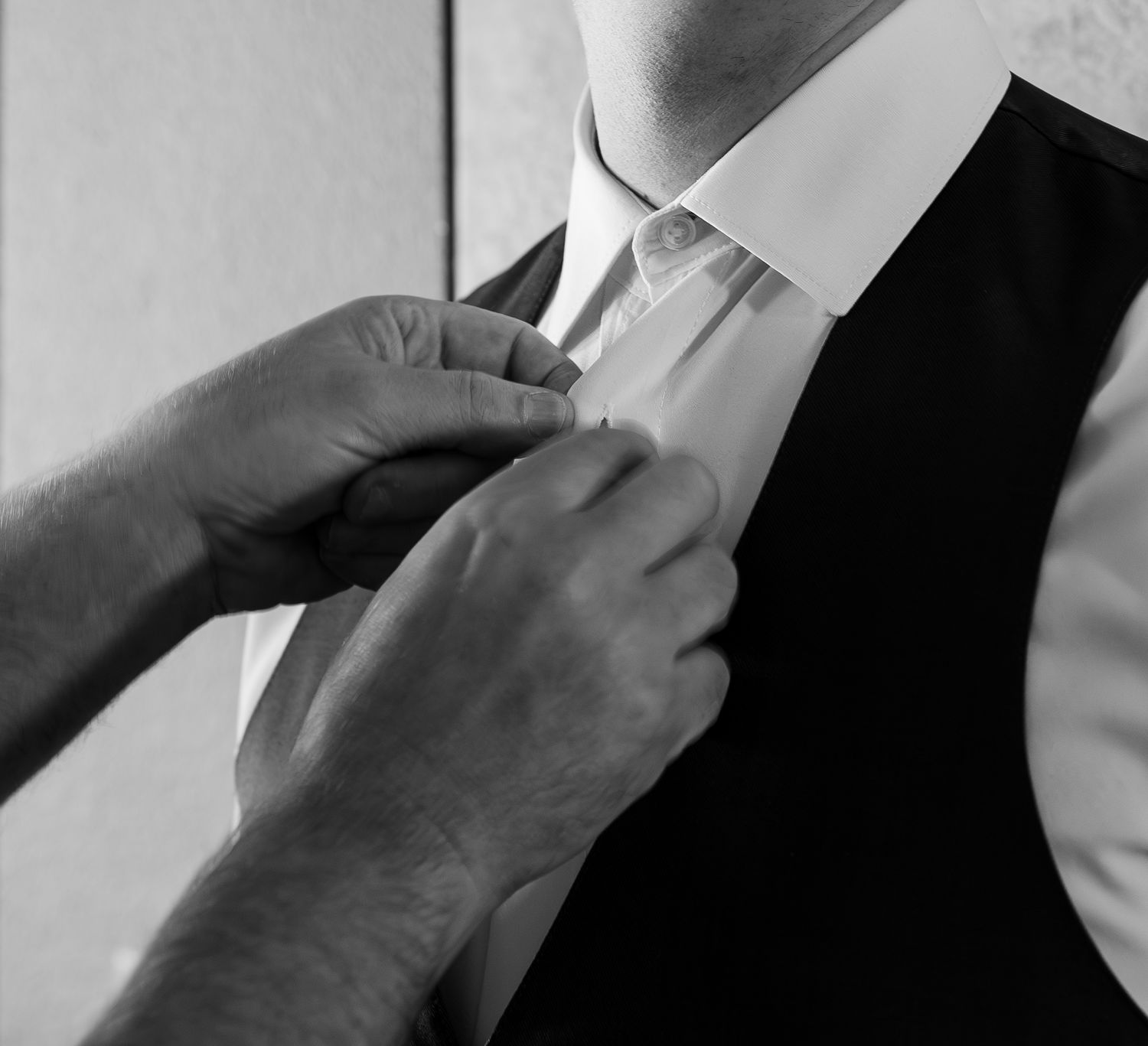 Hands adjusting a boutonniere on a man's black vest and white dress shirt in a black and white photo.