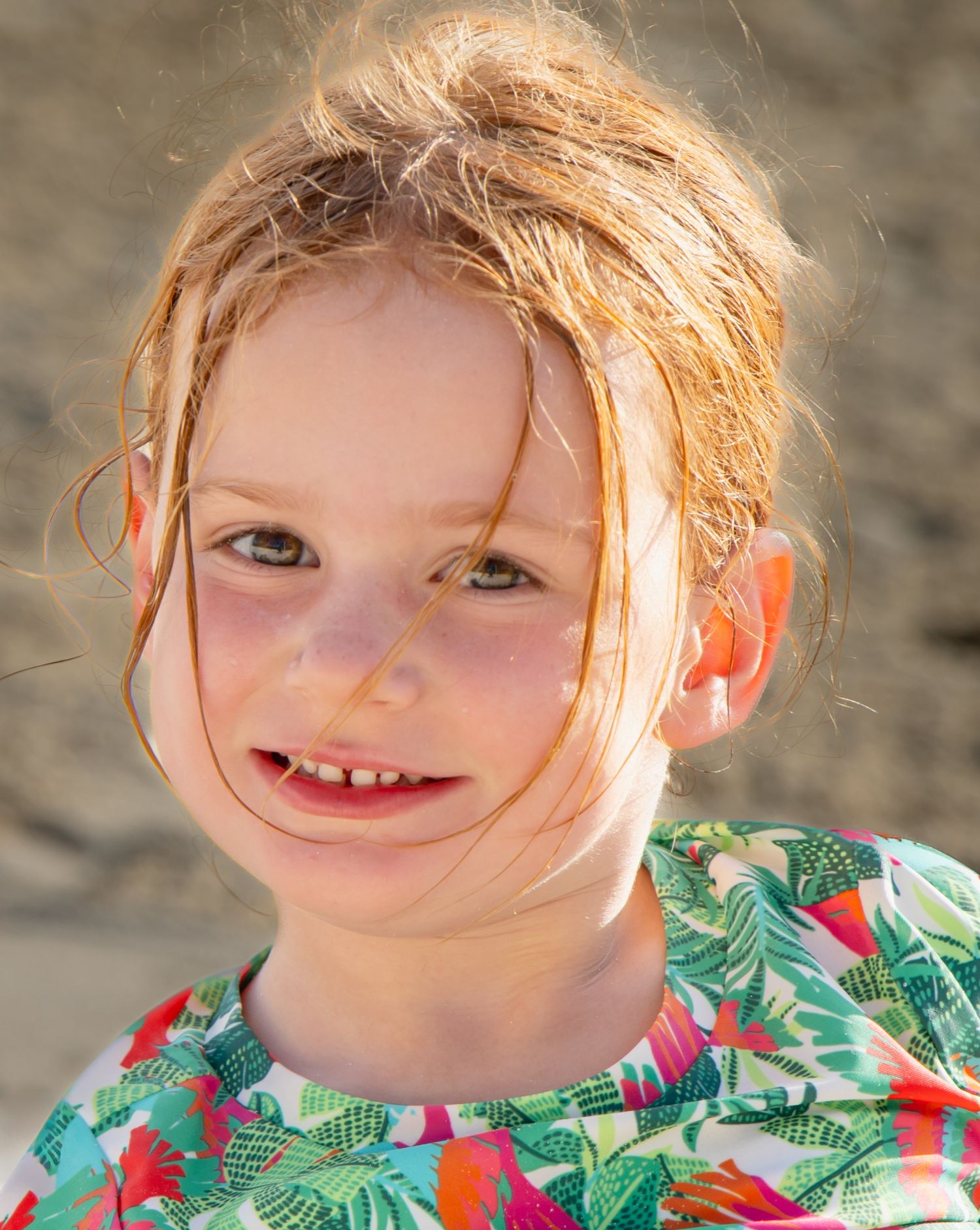 A smiling child with windswept hair wearing a tropical print shirt on a sunny day.