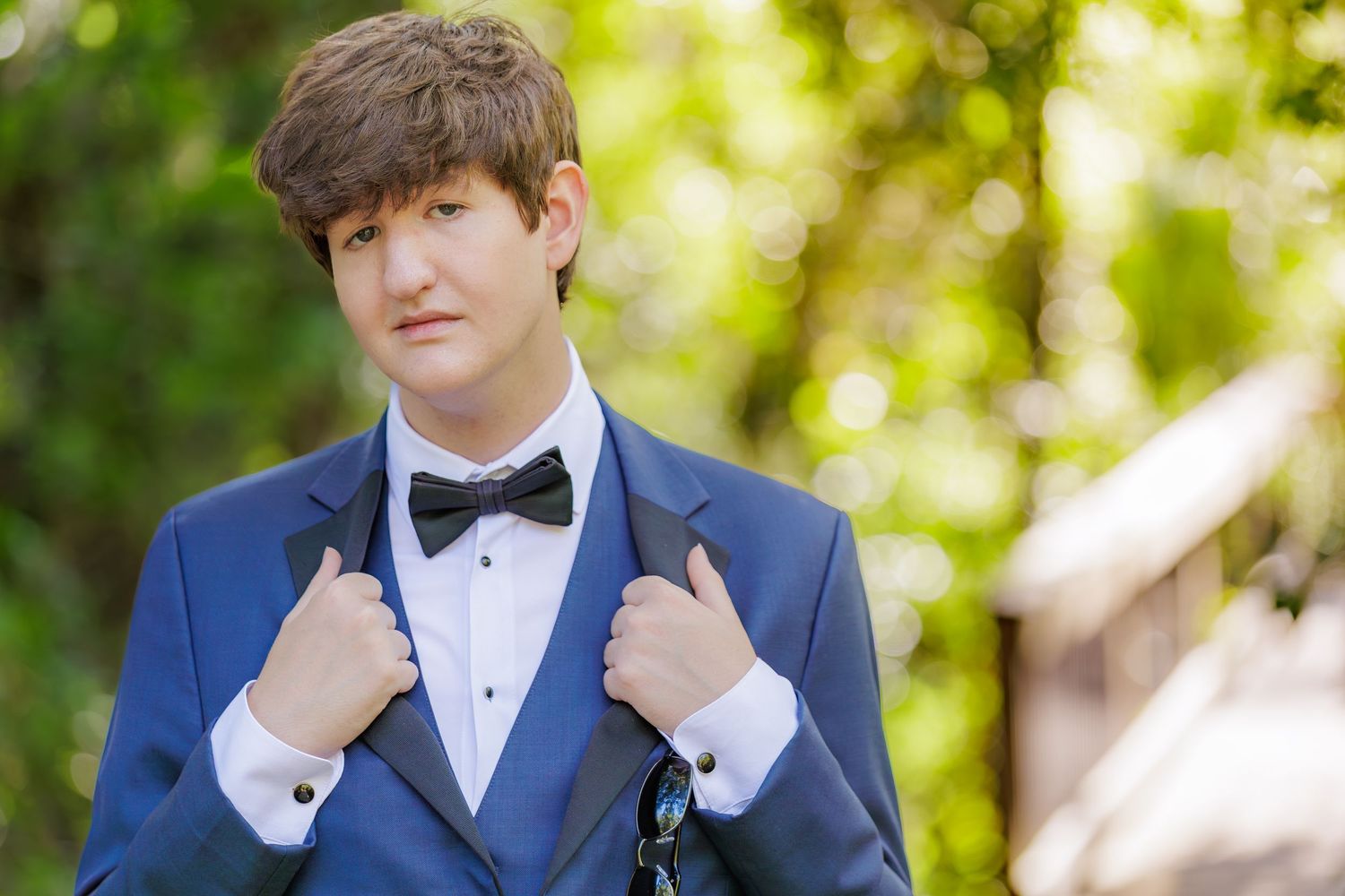 Young man in a blue tuxedo with black bow tie posing outdoors at a formal event.