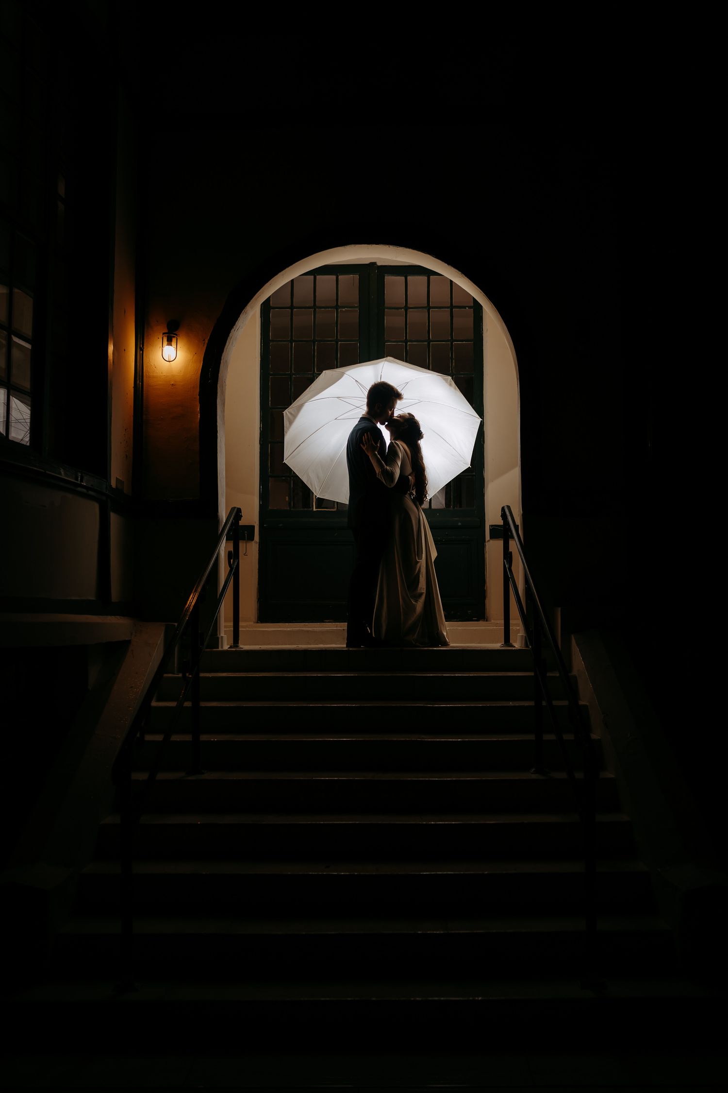 Creative silhouette wedding photo on stairs with umbrella lighting.