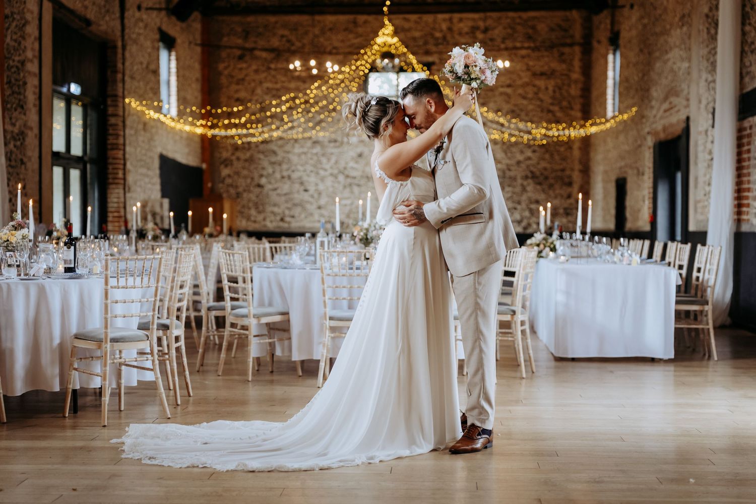 A couple enjoy a portrait together in the main barn under the fairy lights at Granary Estates