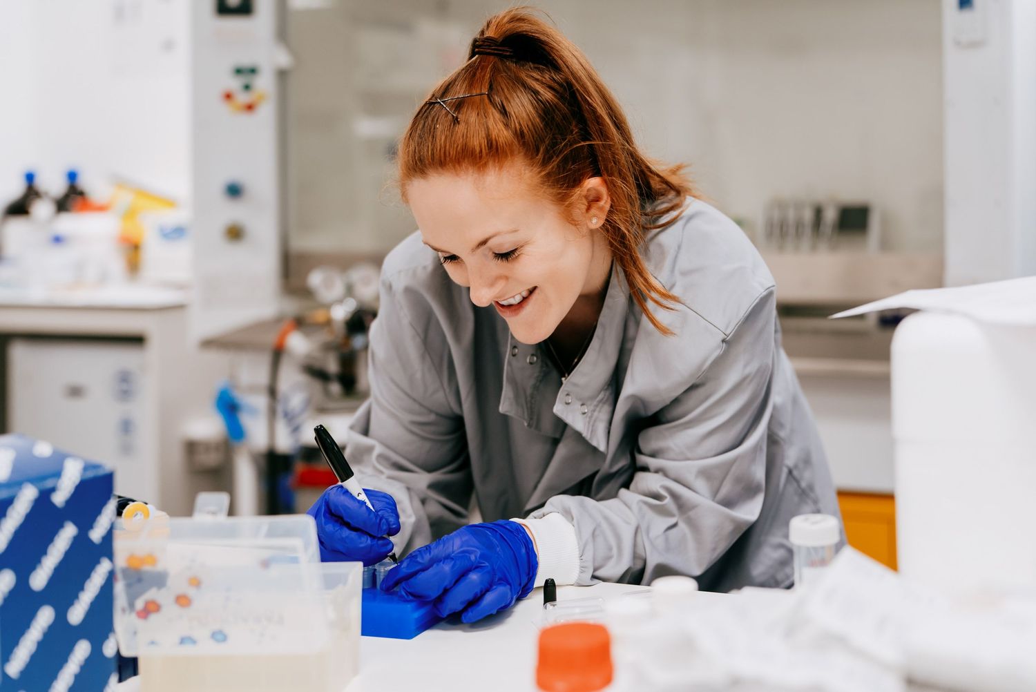 Scientist in lab coat and gloves conducts research with test tubes and laboratory equipment.