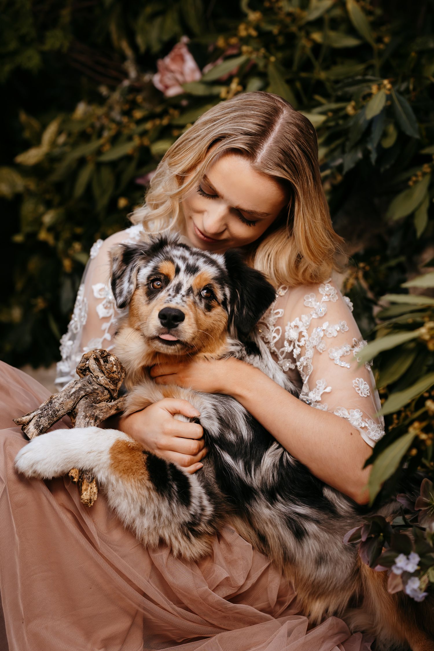 A sweet moment captured between an Australian Shepherd dog and someone in a floral dress surrounded by greenery.