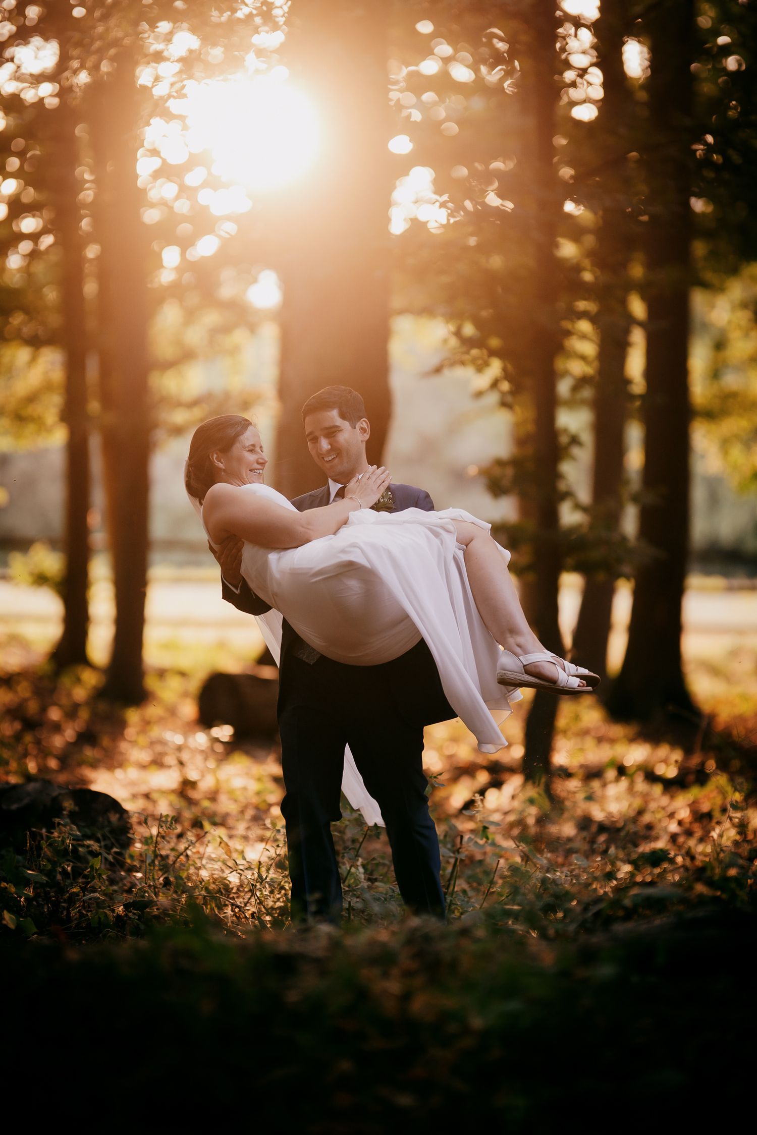 Groom carrying bride in the forest at Lanwades Hall, an iconic Newmarket wedding venue.