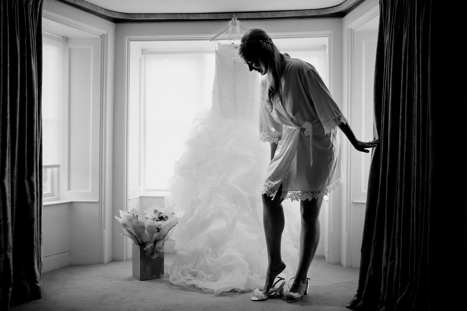 Black and white photo striking silhouette of bride in window during preparations in Norfolk.