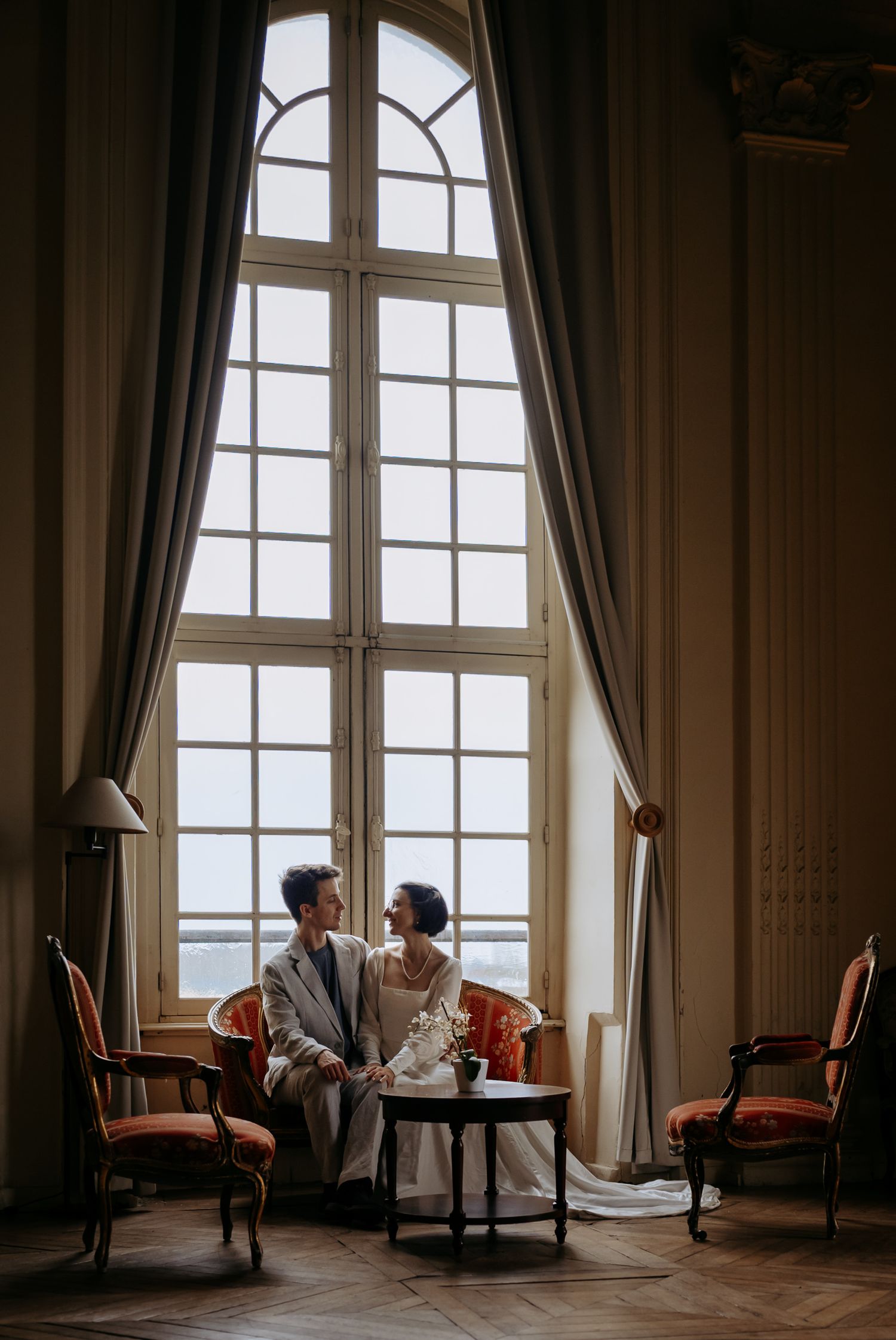 Luxury wedding photo of a couple relaxed on a grand hall bench.