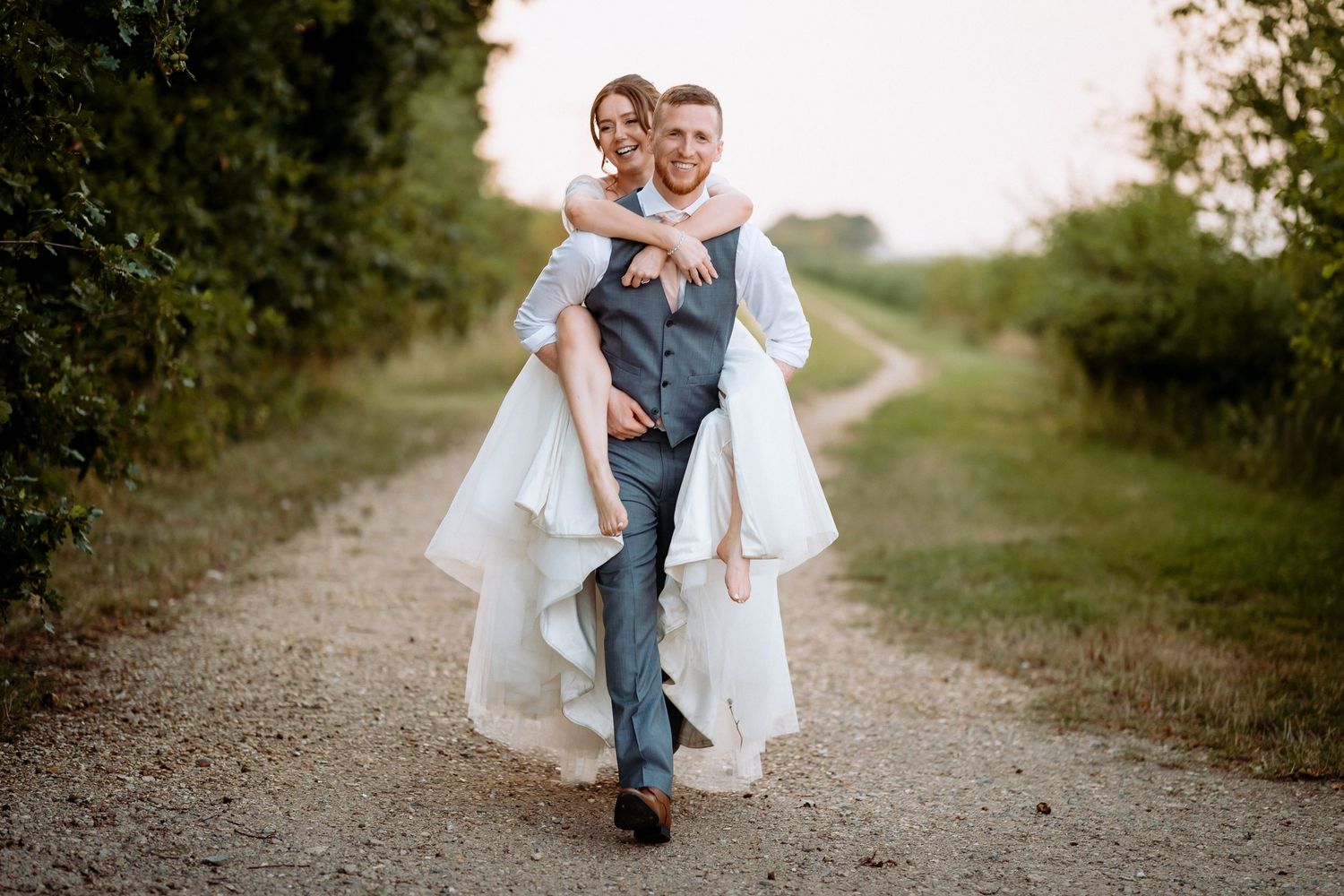 A romantic piggyback wedding photo on a rustic farm path at Bassmead Manor.