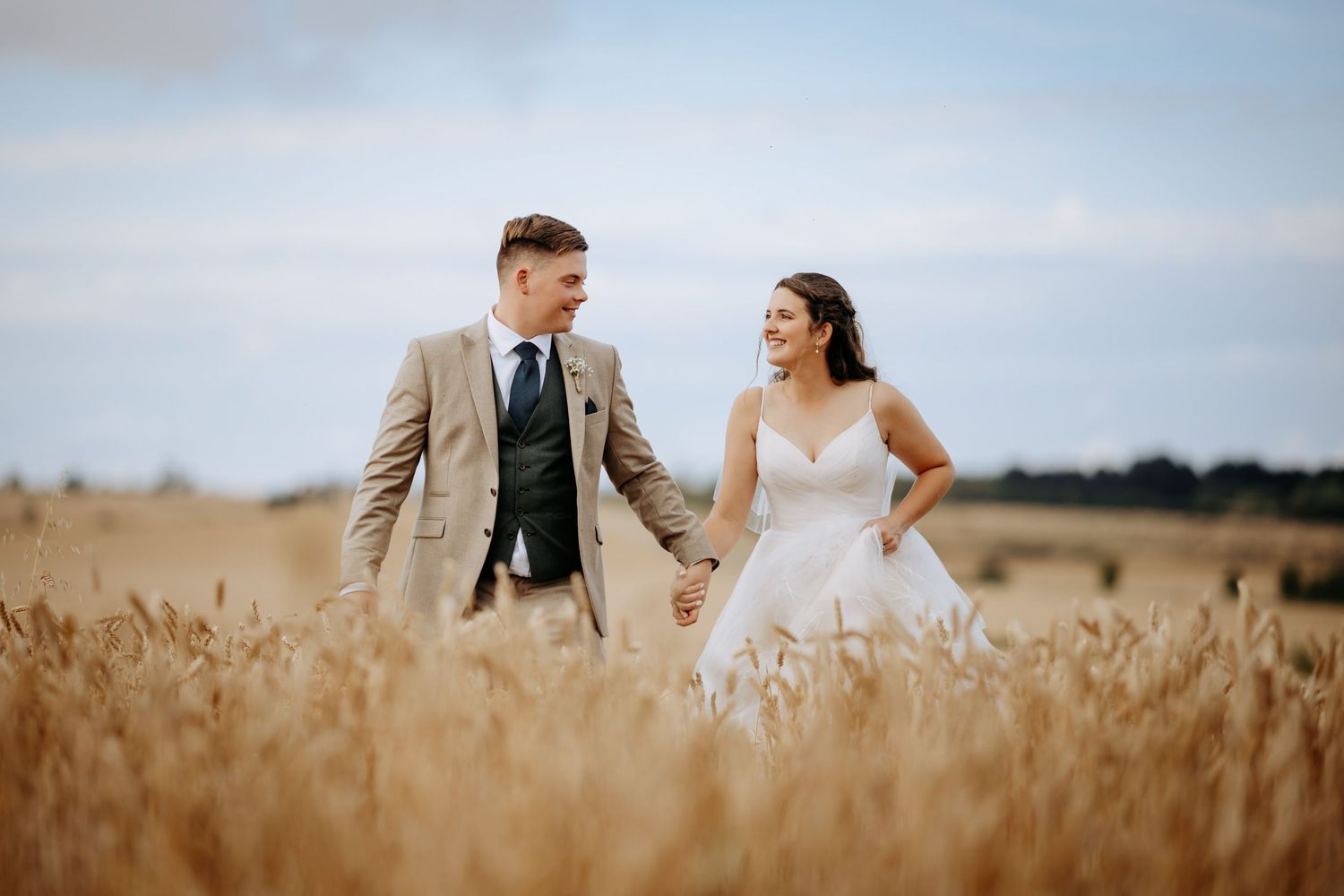 A bride and groom share a romantic moment while walking through a golden wheat field at sunset.