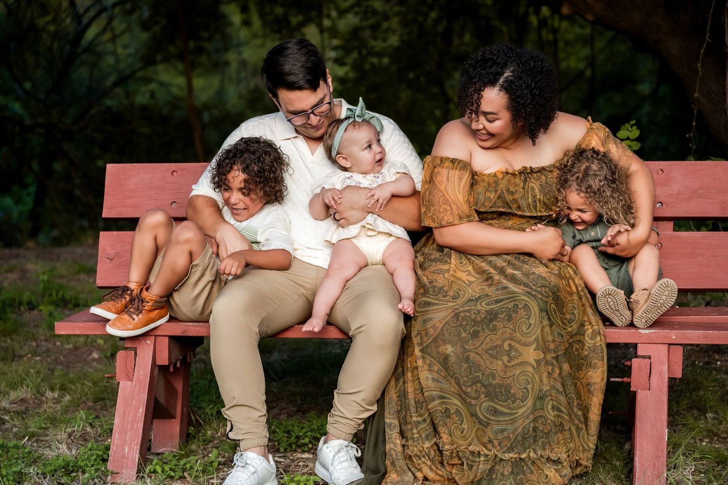 Family of five sitting on a red bench in a lush green park, sharing a joyful moment.