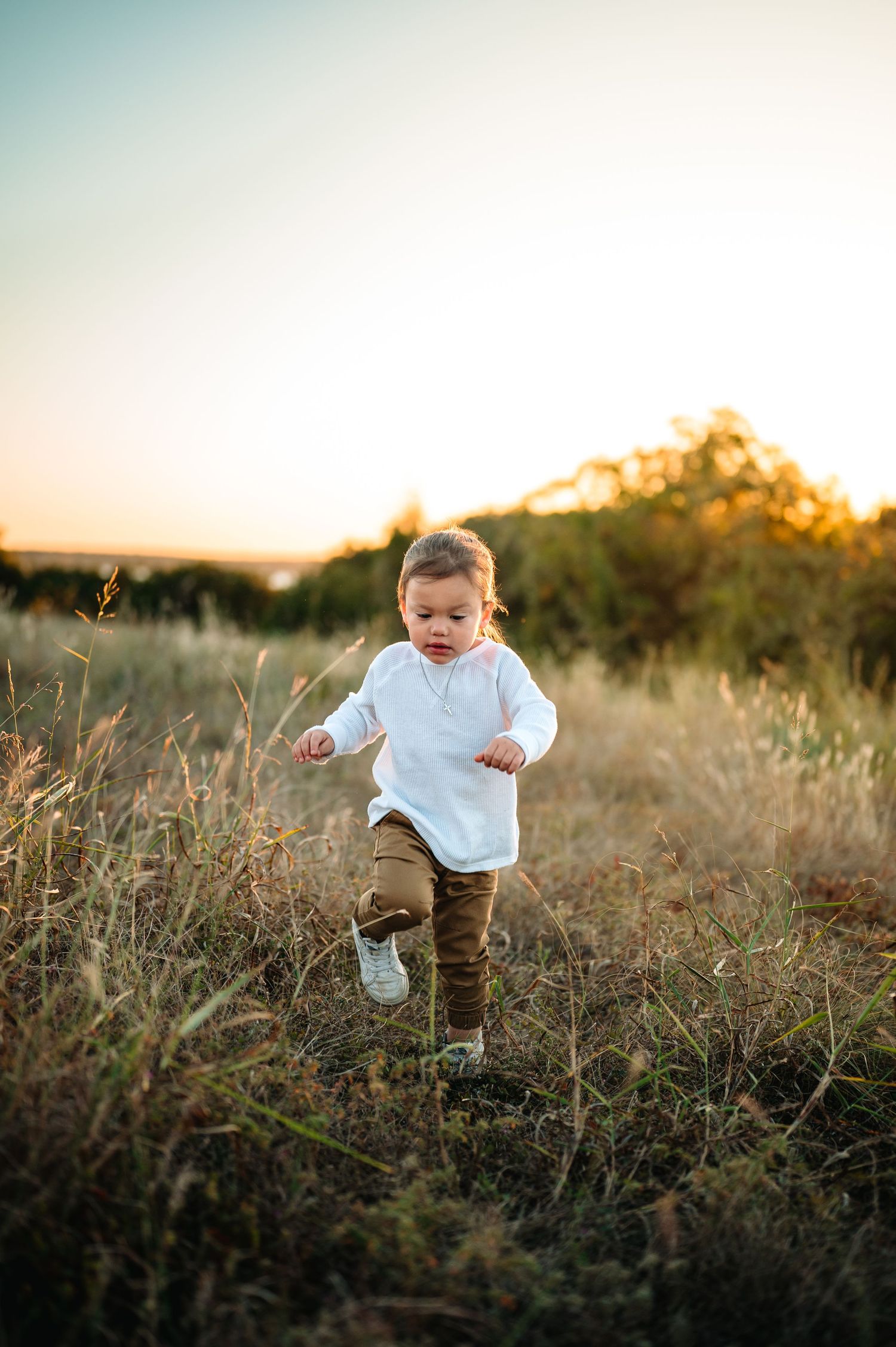 Toddler in a white shirt running through a golden field at sunset in nature.