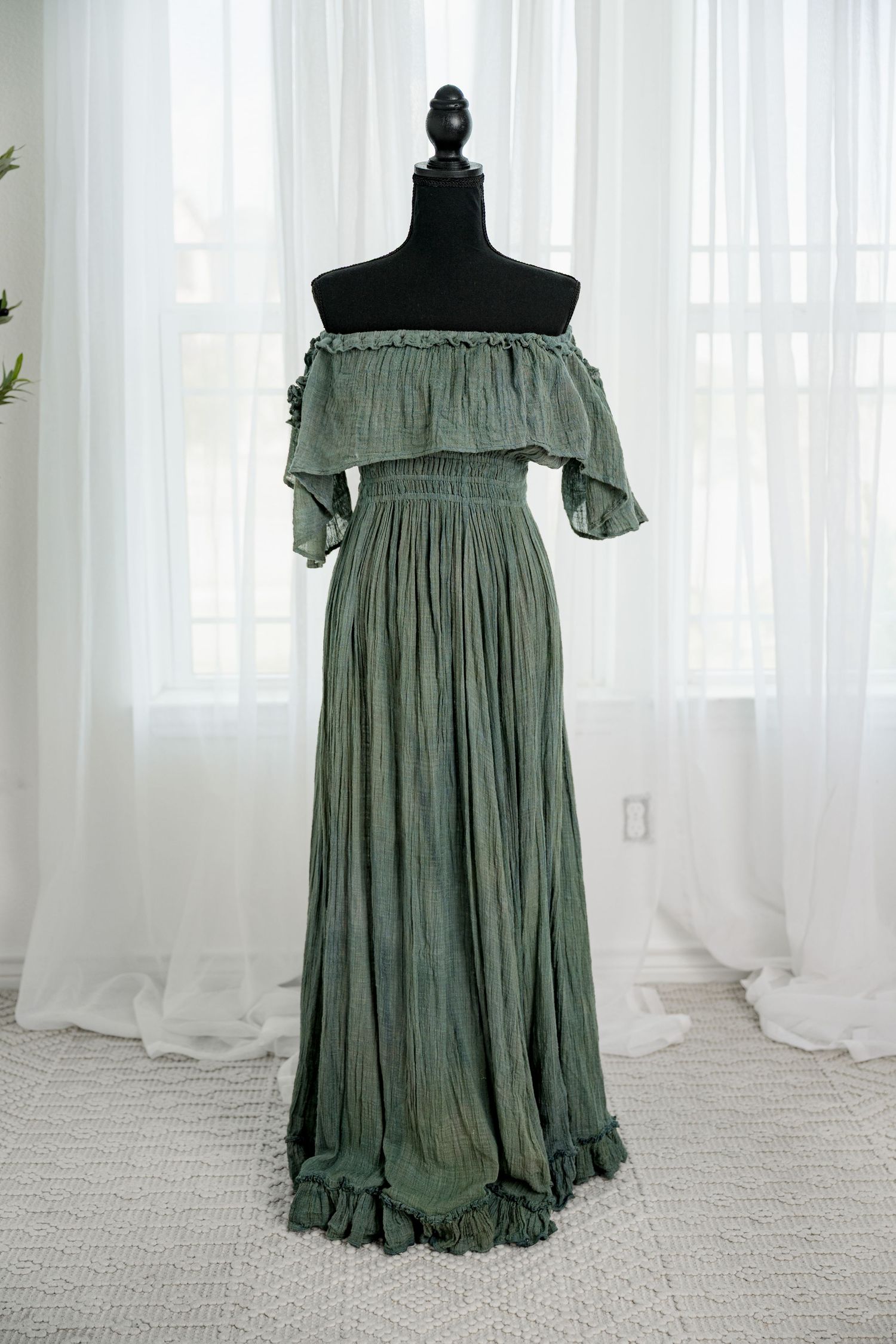 Olive green off-shoulder smocked boho maxi dress with ruffled hem on a black mannequin.
