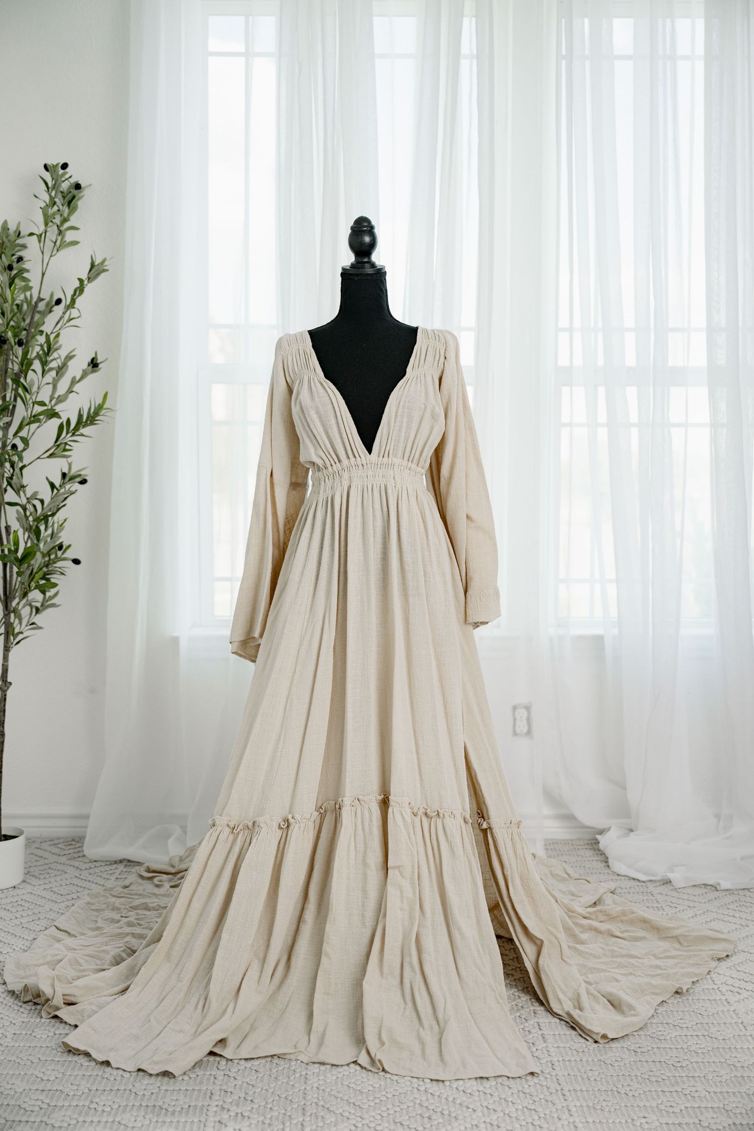 Beige deep V-neck long sleeve tiered boho maxi dress with train on a black mannequin.