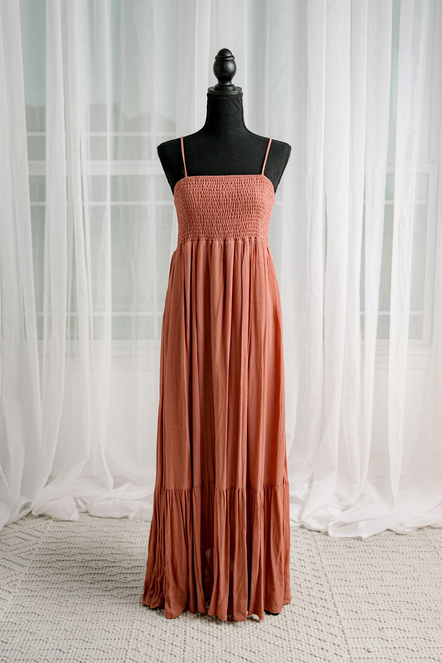 Terracotta smocked bodice spaghetti strap tiered maxi dress on mannequin.