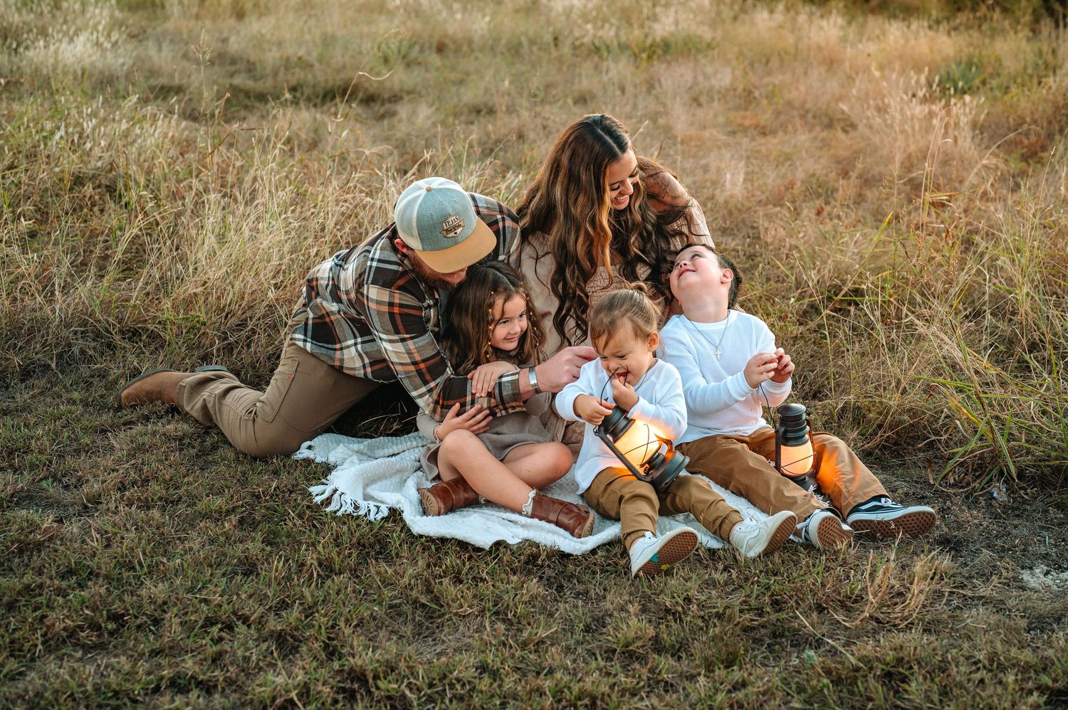 Family of five sitting together on a white blanket in a golden field during autumn.