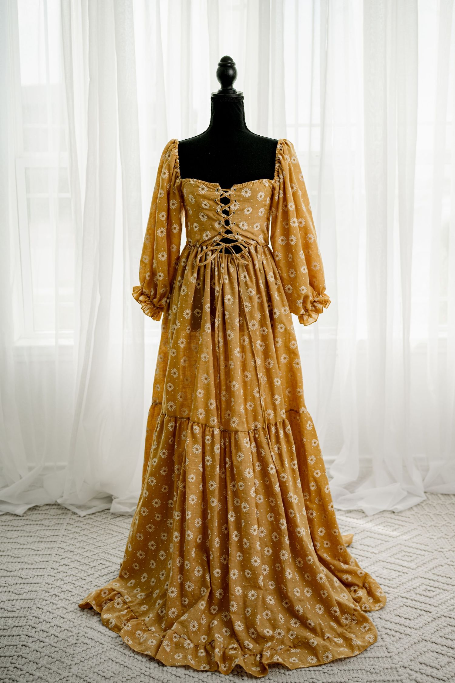 Golden floral maxi dress with puff sleeves, lace-up bodice, and tiered skirt displayed on a black mannequin.