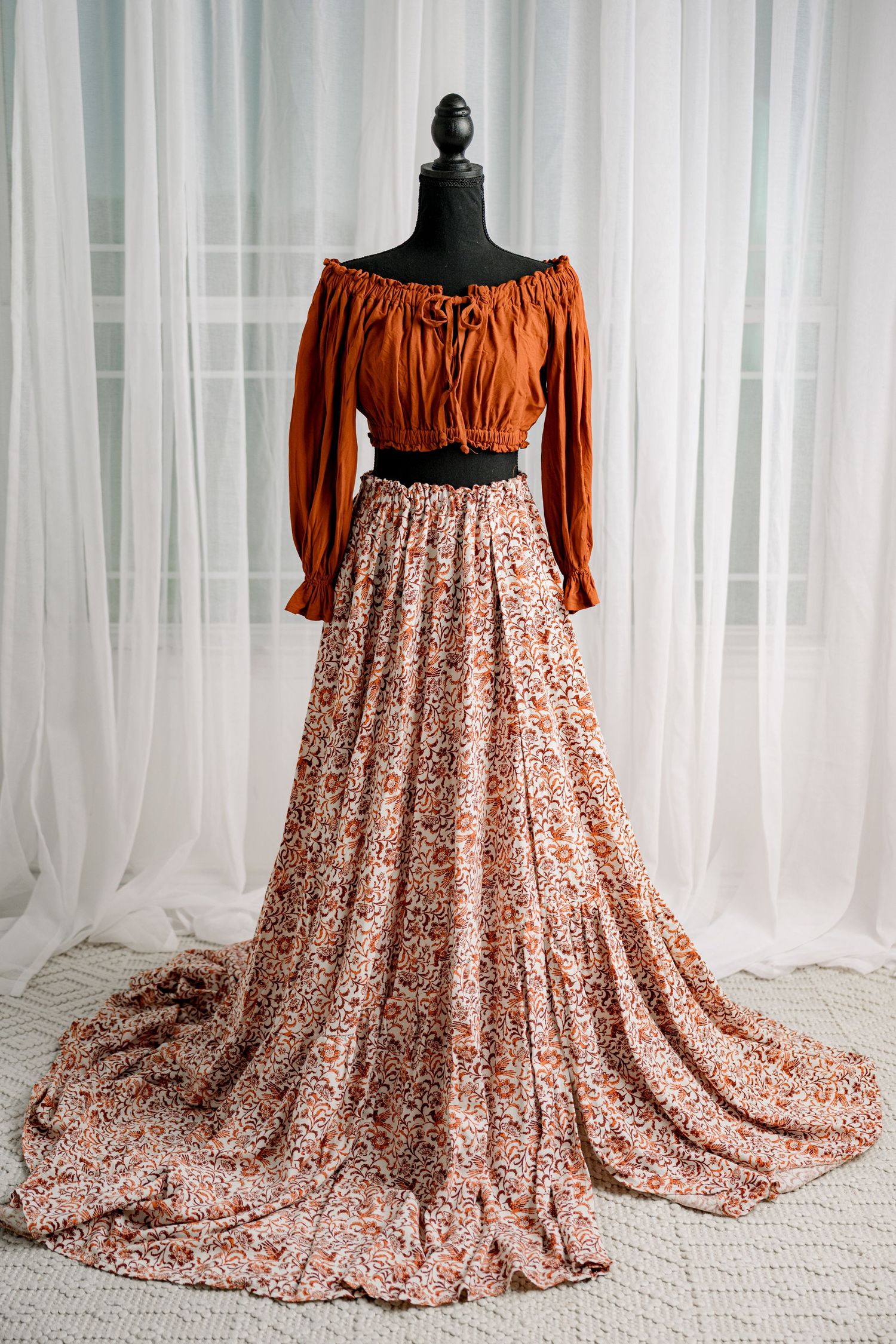 Rust off-shoulder top with floral print maxi skirt two-piece set on mannequin.