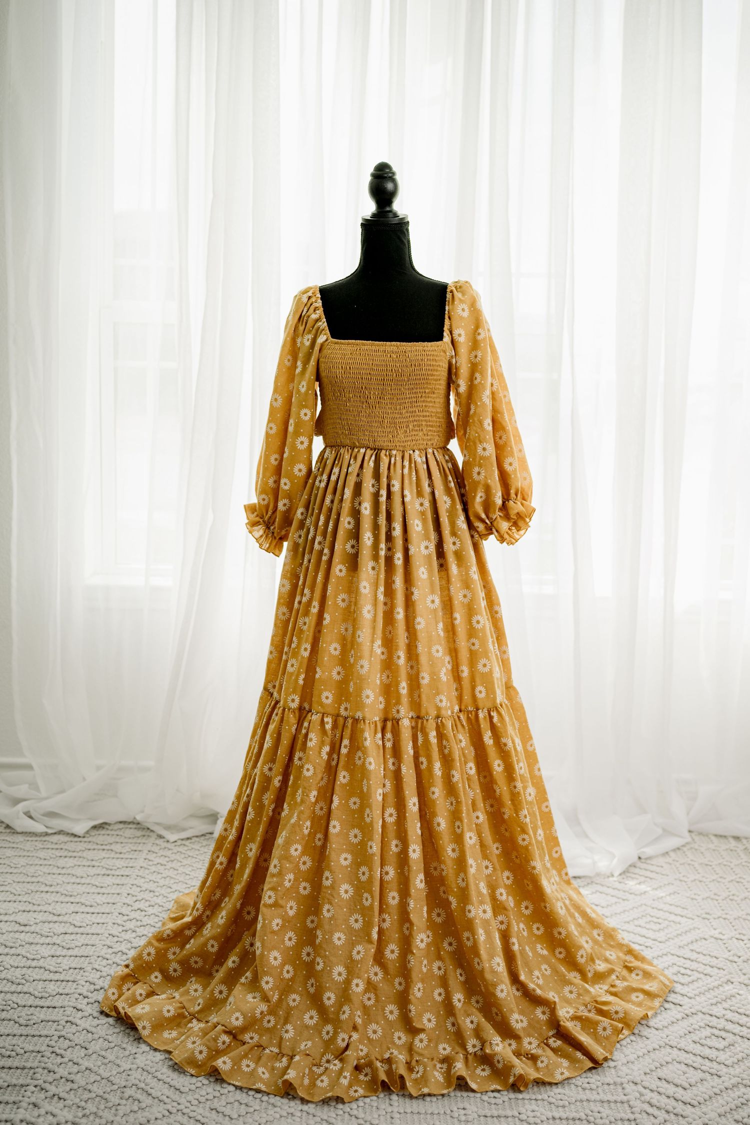 Golden floral smocked bodice maxi dress with puff sleeves and tiered skirt on mannequin.