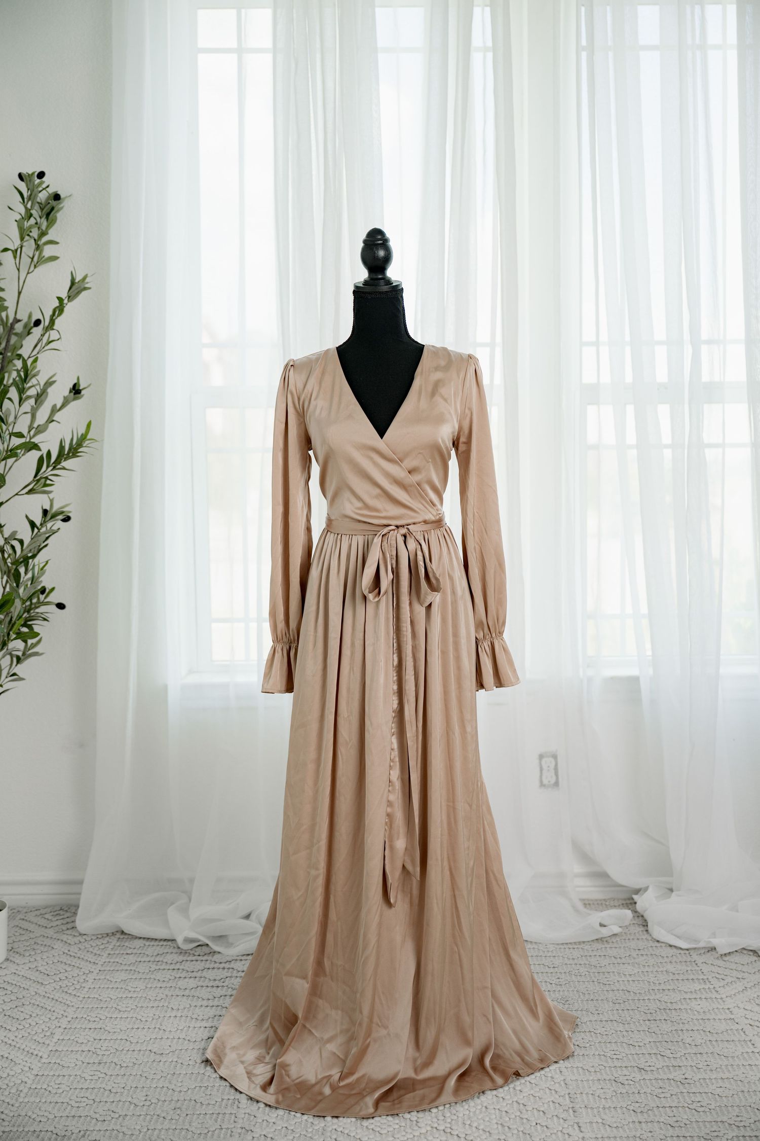 Champagne satin long sleeve wrap maxi dress with tie waist on a black mannequin.